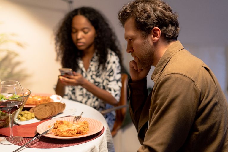 Two adults sitting at a table, enjoying a meal with wine in a cozy indoor setting.