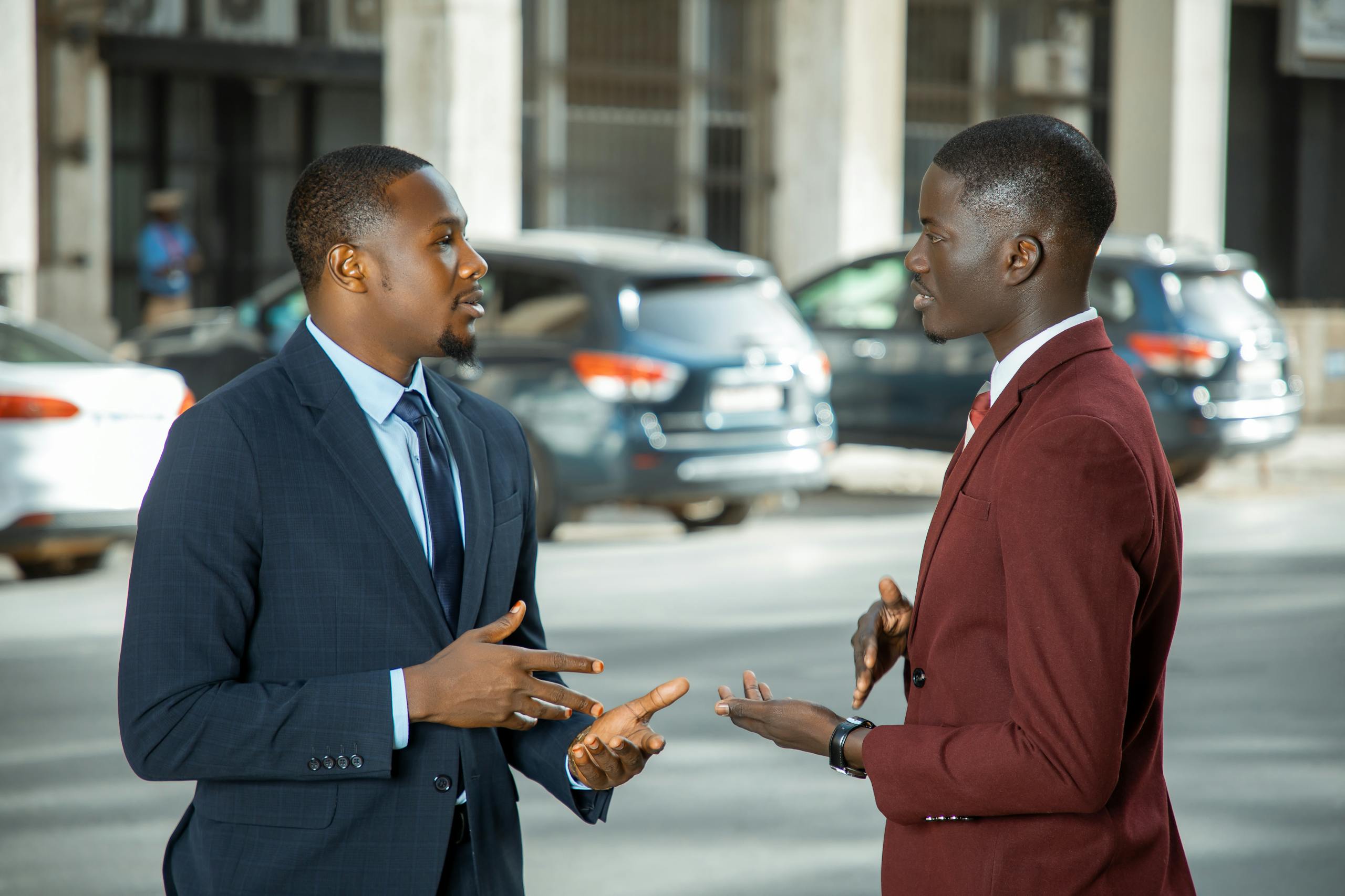 Two African businessmen in formal suits have a discussion on a city street in Dakar, Senegal.