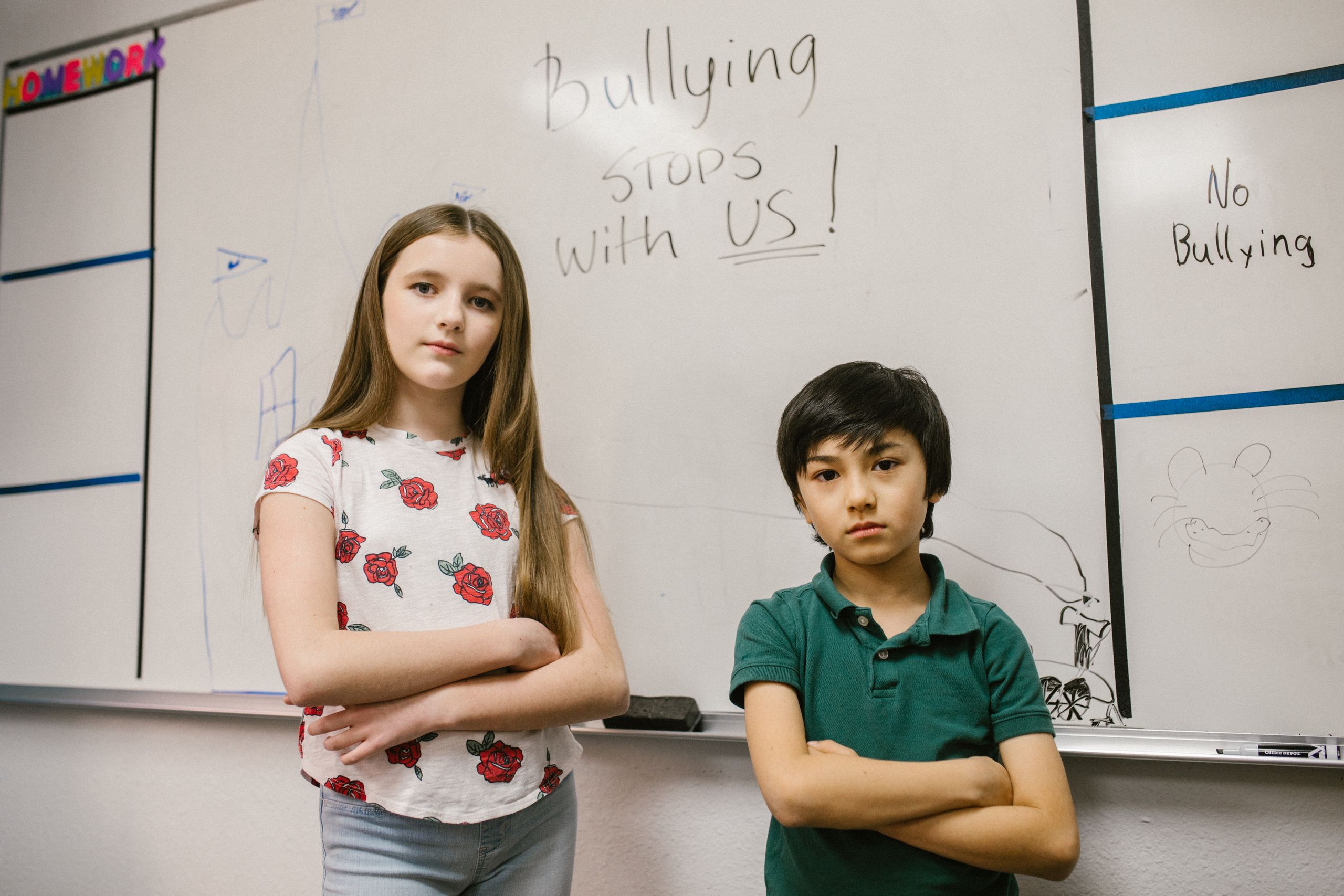 Two children standing confidently in front of anti-bullying message on classroom whiteboard.