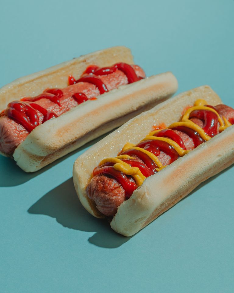 Two delicious hot dogs topped with ketchup and mustard on a blue background.