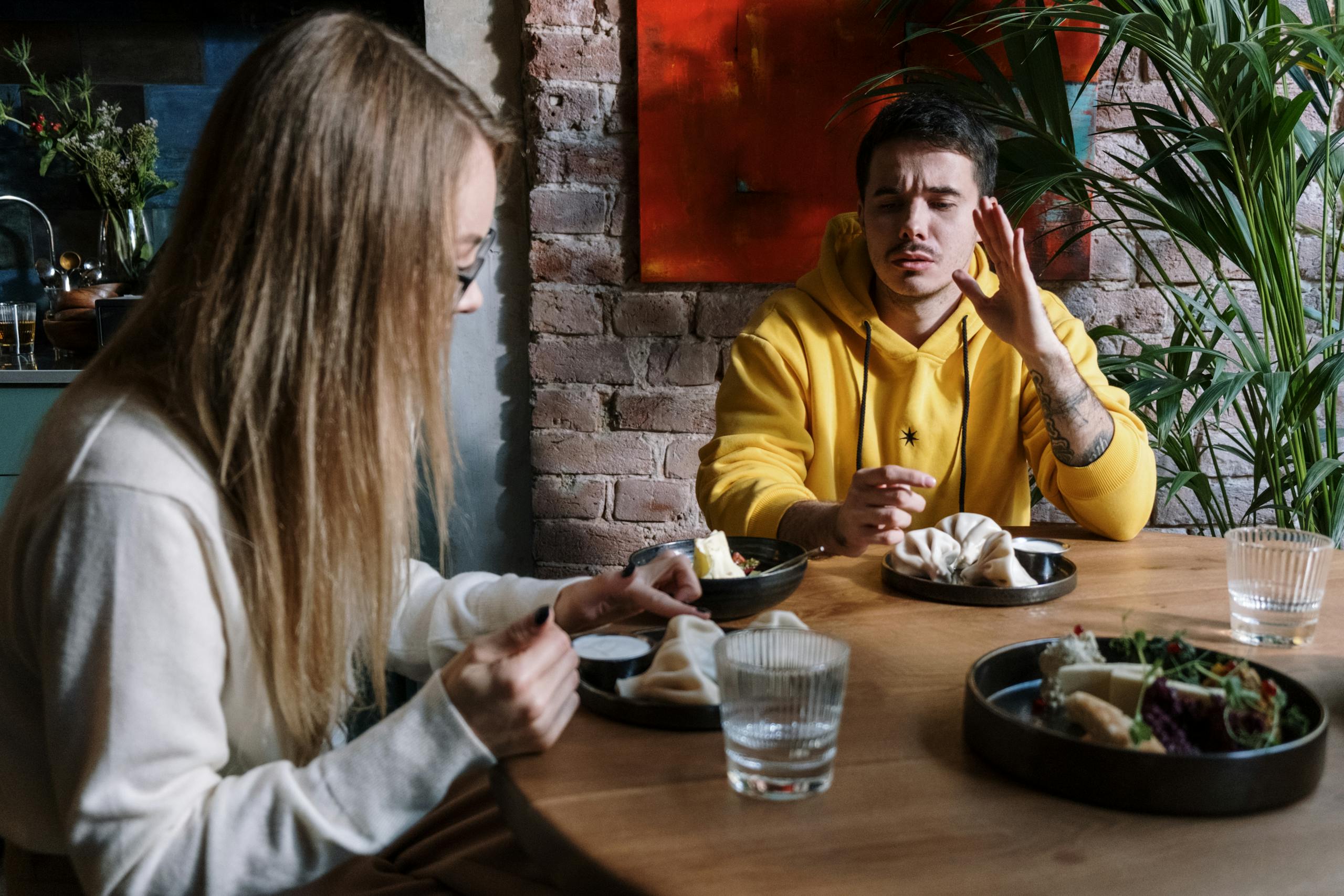 Two friends enjoy a meal indoors using sign language to communicate, highlighting togetherness and nonverbal communication.