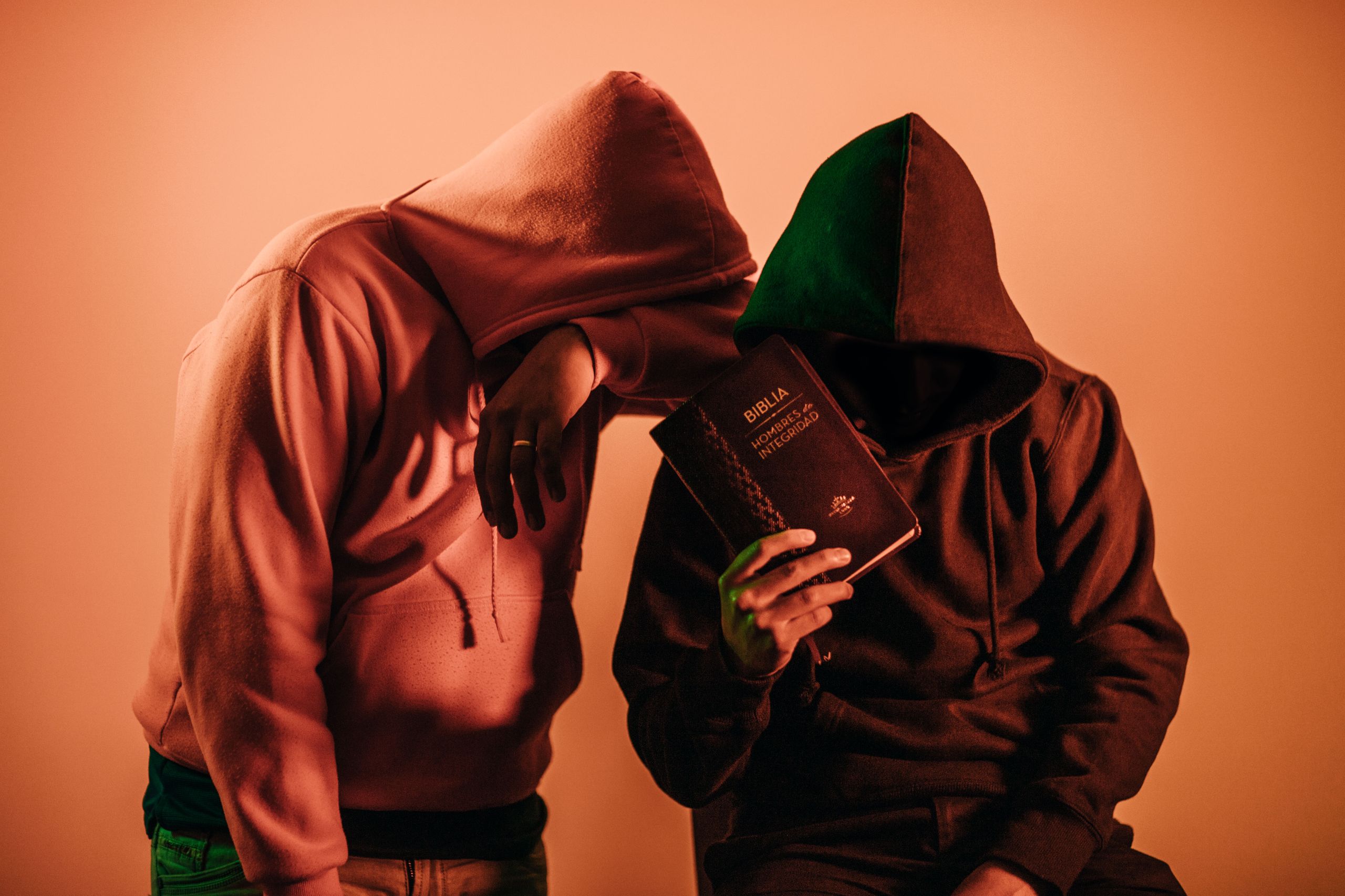 Two hooded figures holding a Bible, conveying mystery and faith.