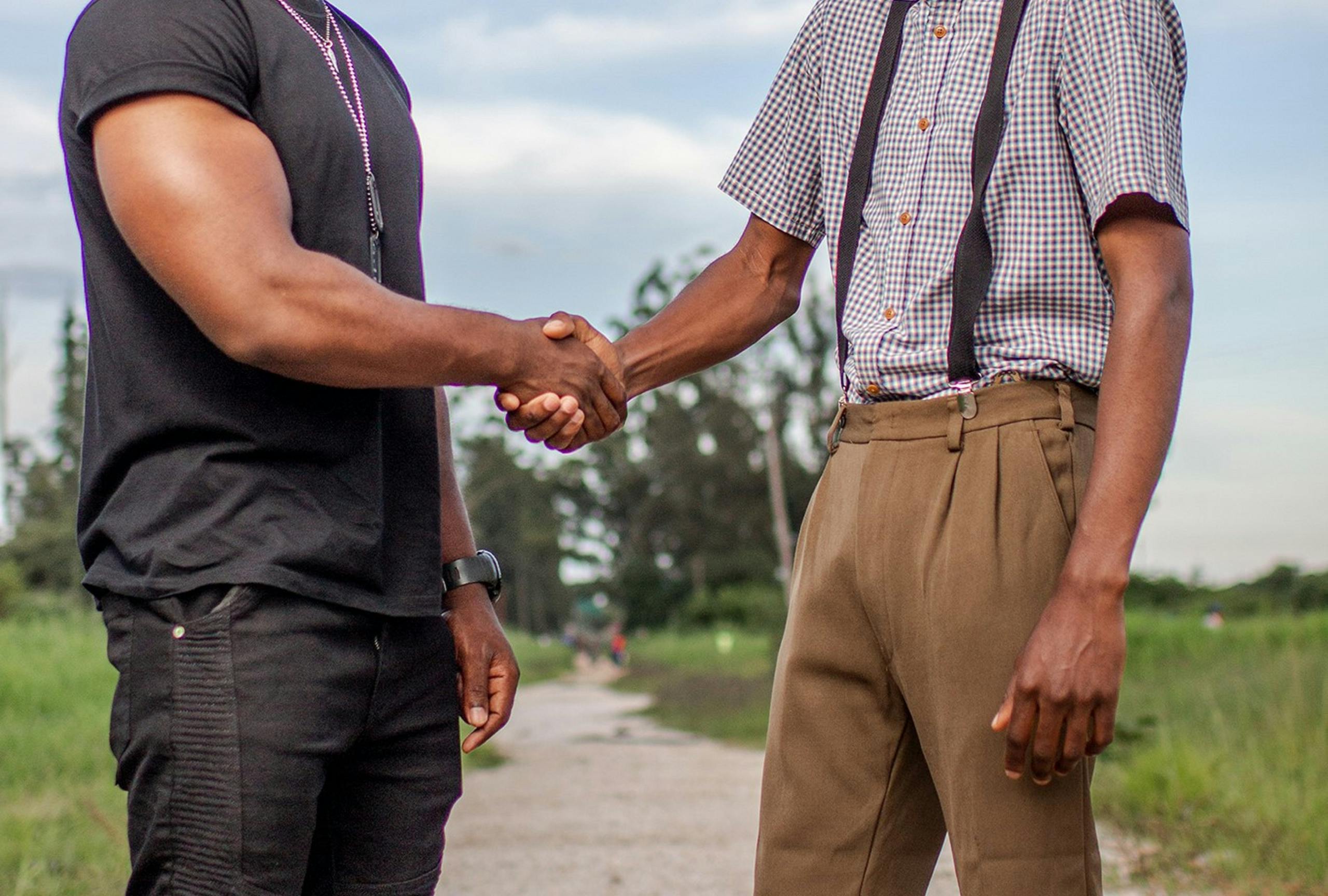 Two men shaking hands outdoors in Lusaka, Zambia. Captures cooperation and agreement.