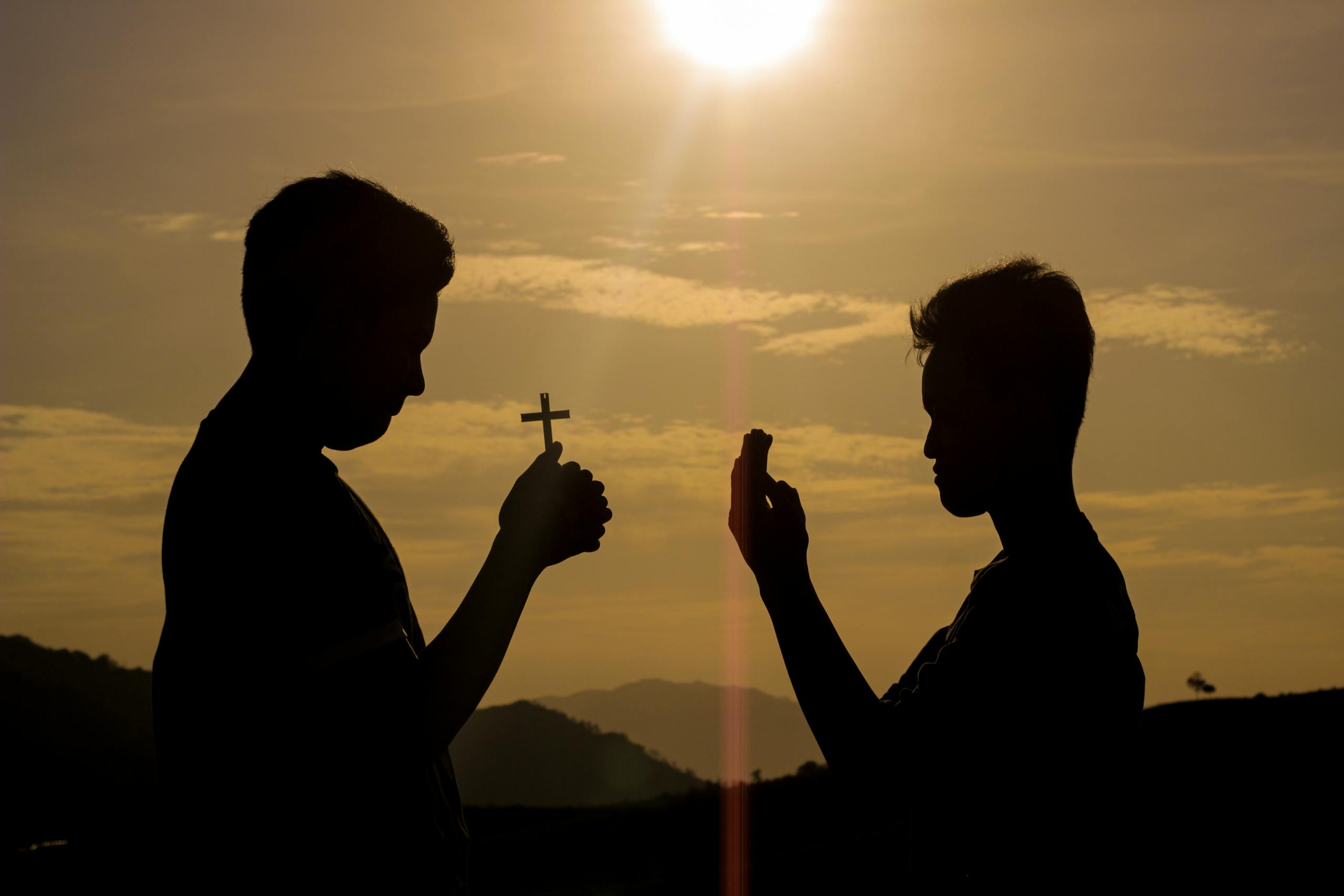 Two men silhouetted against a sunset sky, one holding a cross, symbolizing faith and spirituality.