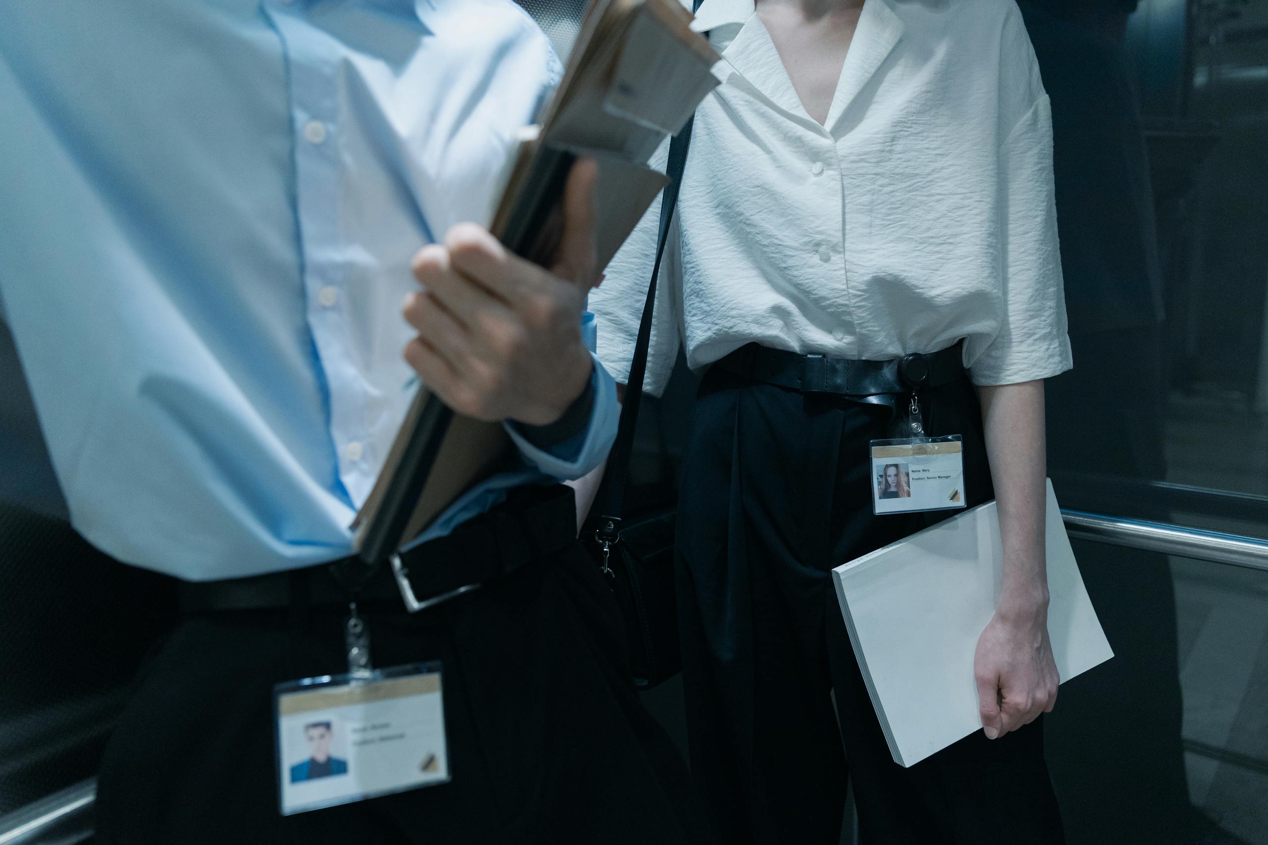 Two professionals in an elevator carrying documents, showcasing office attire.