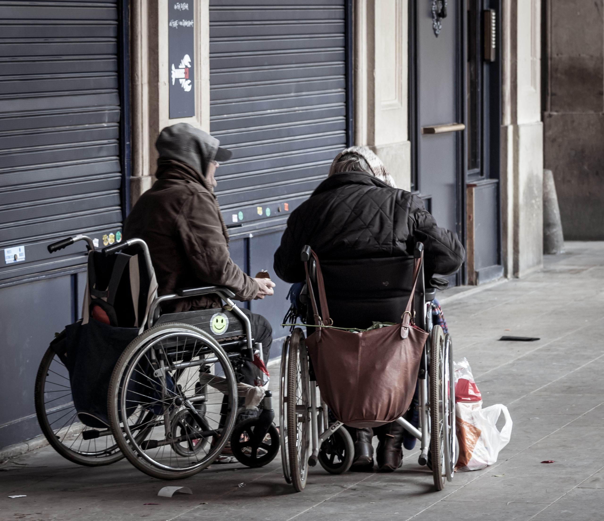Two senior adults in wheelchairs socializing outdoors in winter attire.