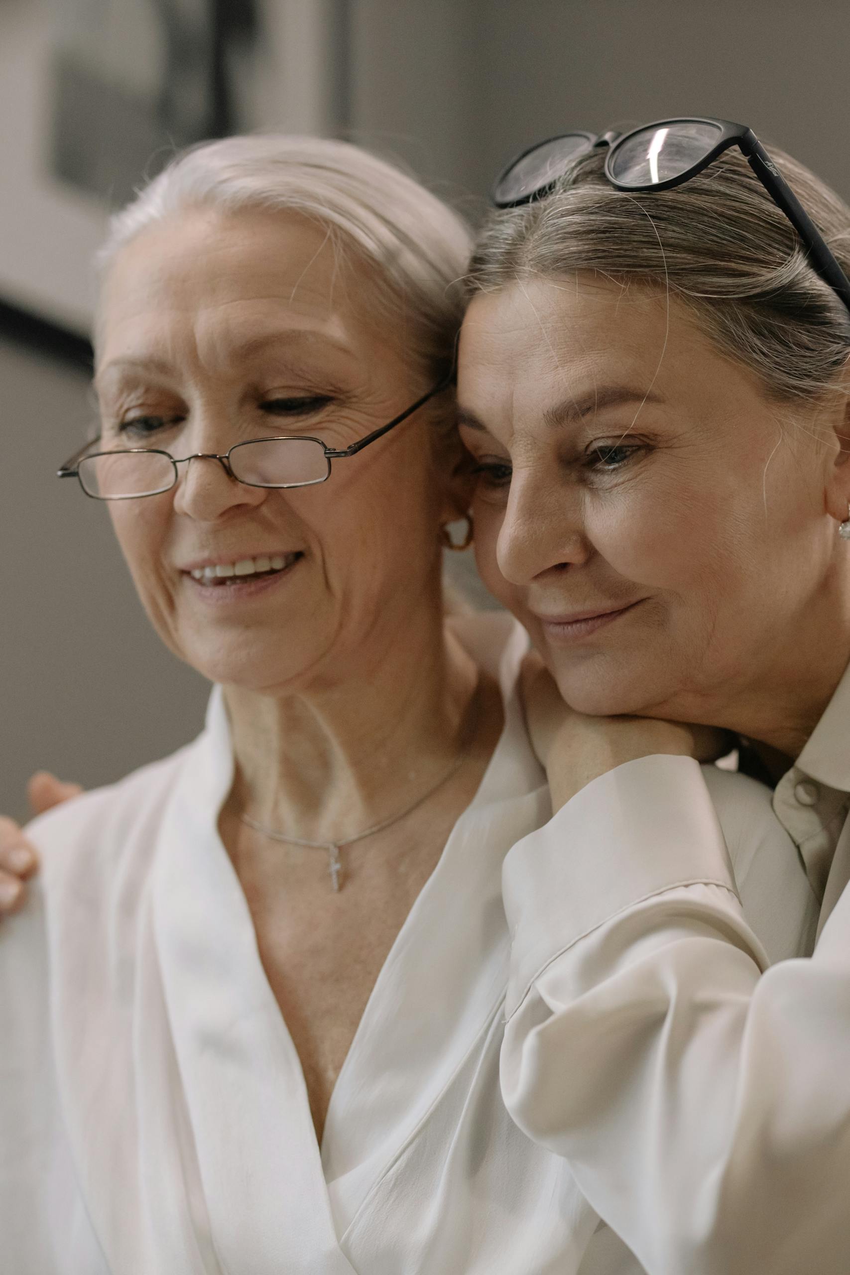 Two senior women embracing and smiling indoors, showcasing friendship and joy.