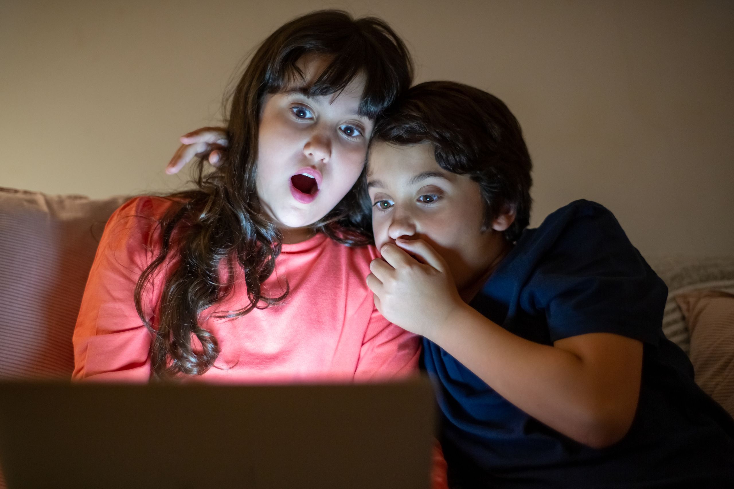 Two siblings experiencing a shocking moment while watching a tablet together at night.