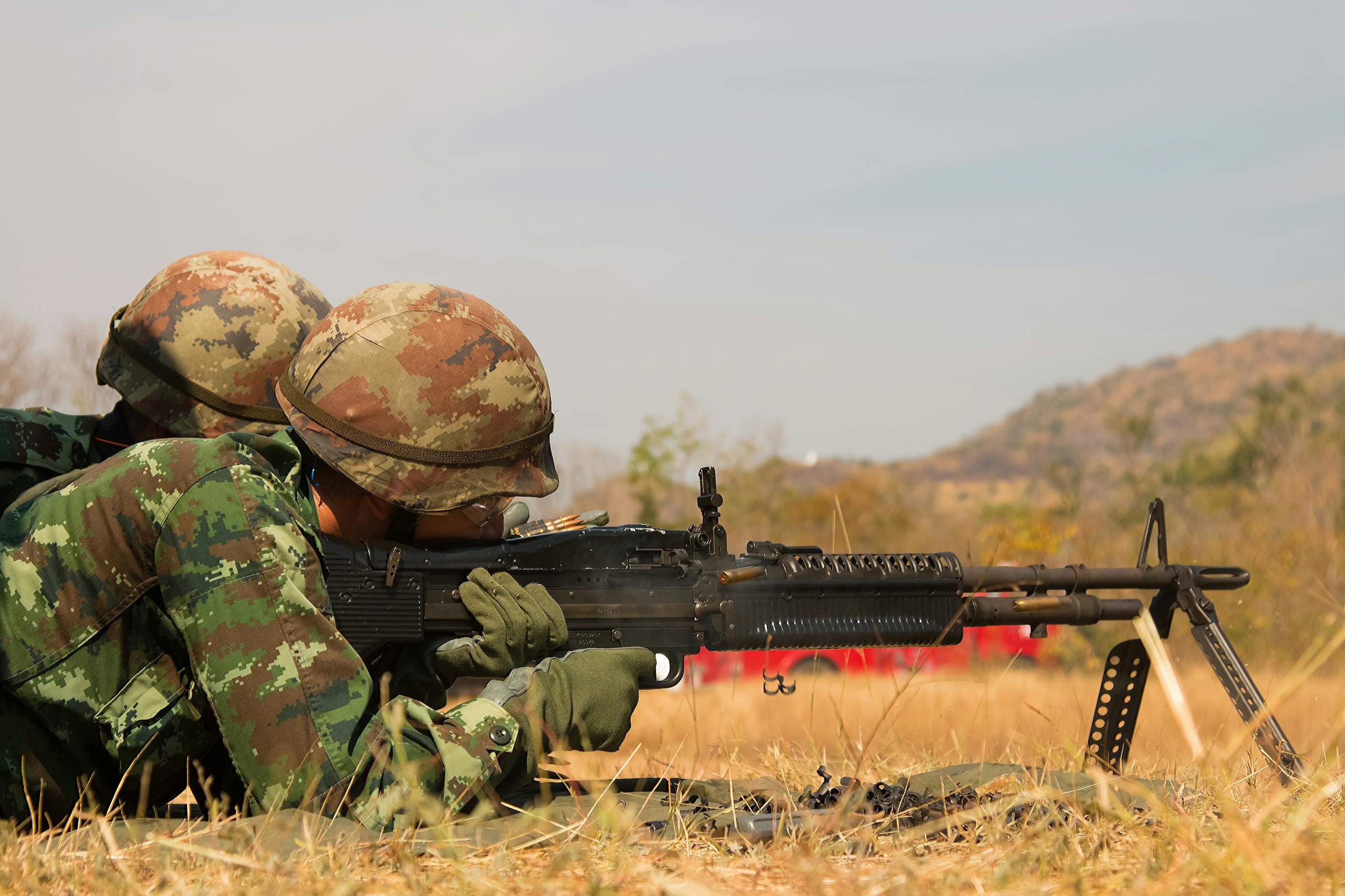 Two soldiers in camouflage uniforms practicing on a field with a machine gun in combat training.