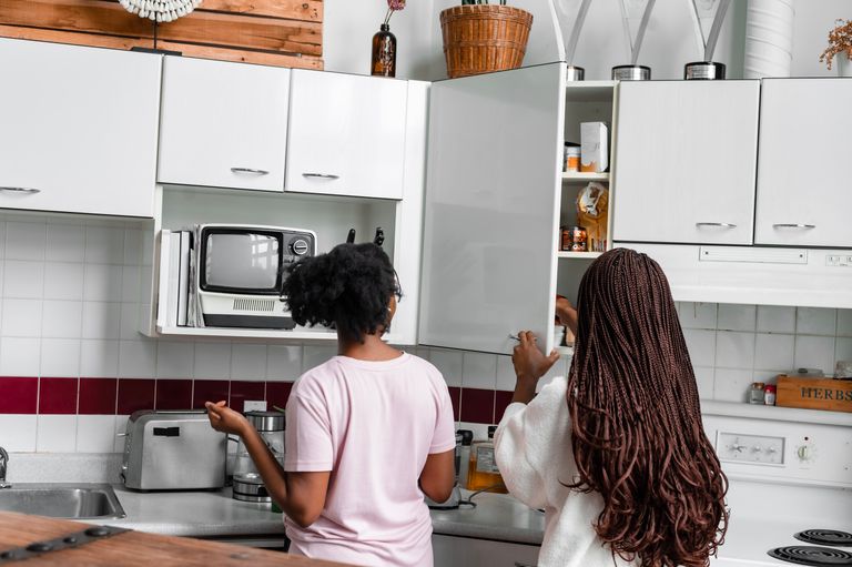 Two women organizing kitchen cabinets in a modern home kitchen with appliances and fixtures.