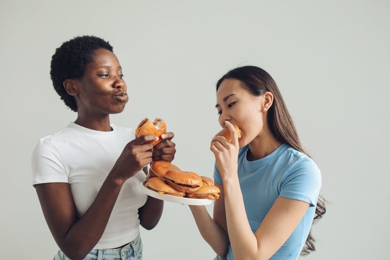 Two women sharing a moment eating burgers indoors, highlighting enjoyment and camaraderie.