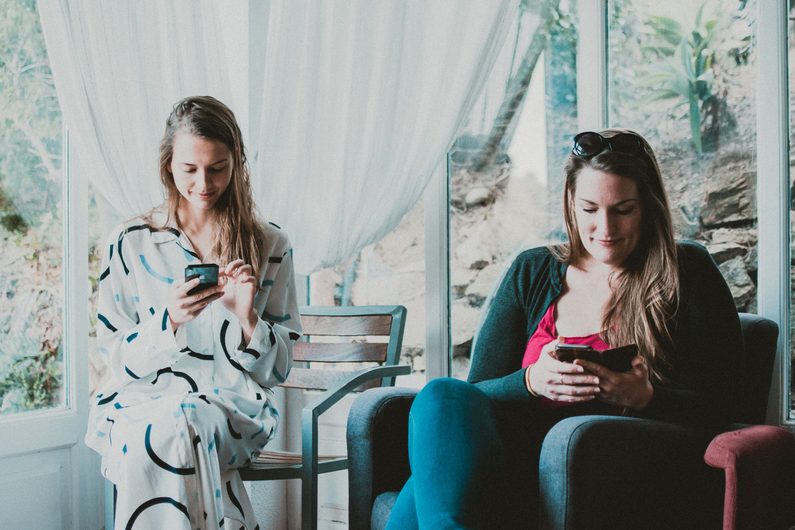 Two women sitting indoors, using smartphones and enjoying a relaxed environment.