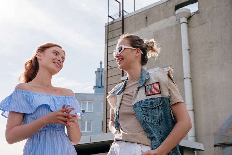 Two women smiling and chatting on a sunlit urban rooftop in summer.