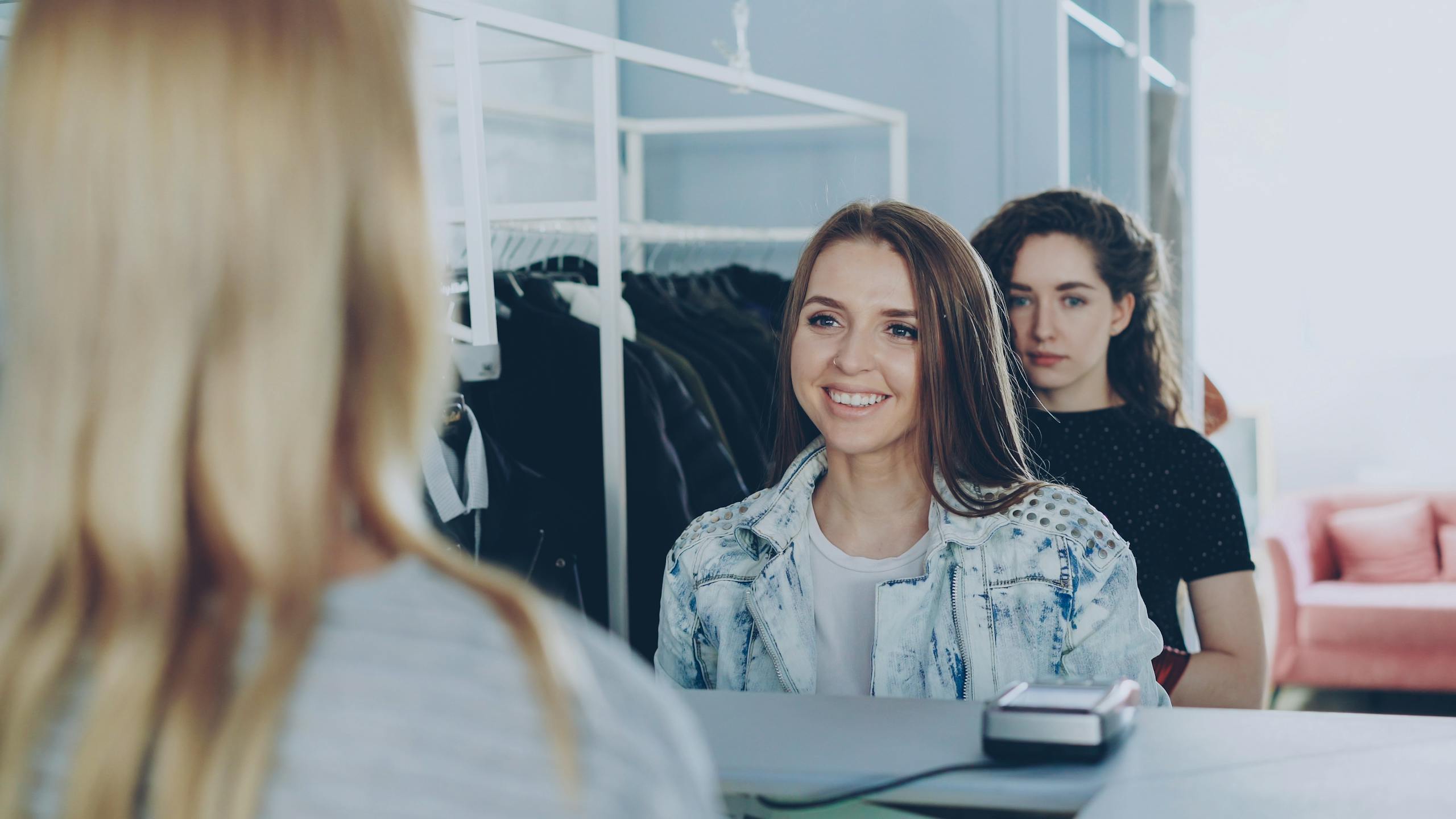 Two young women shopping and interacting with cashier in clothing store.