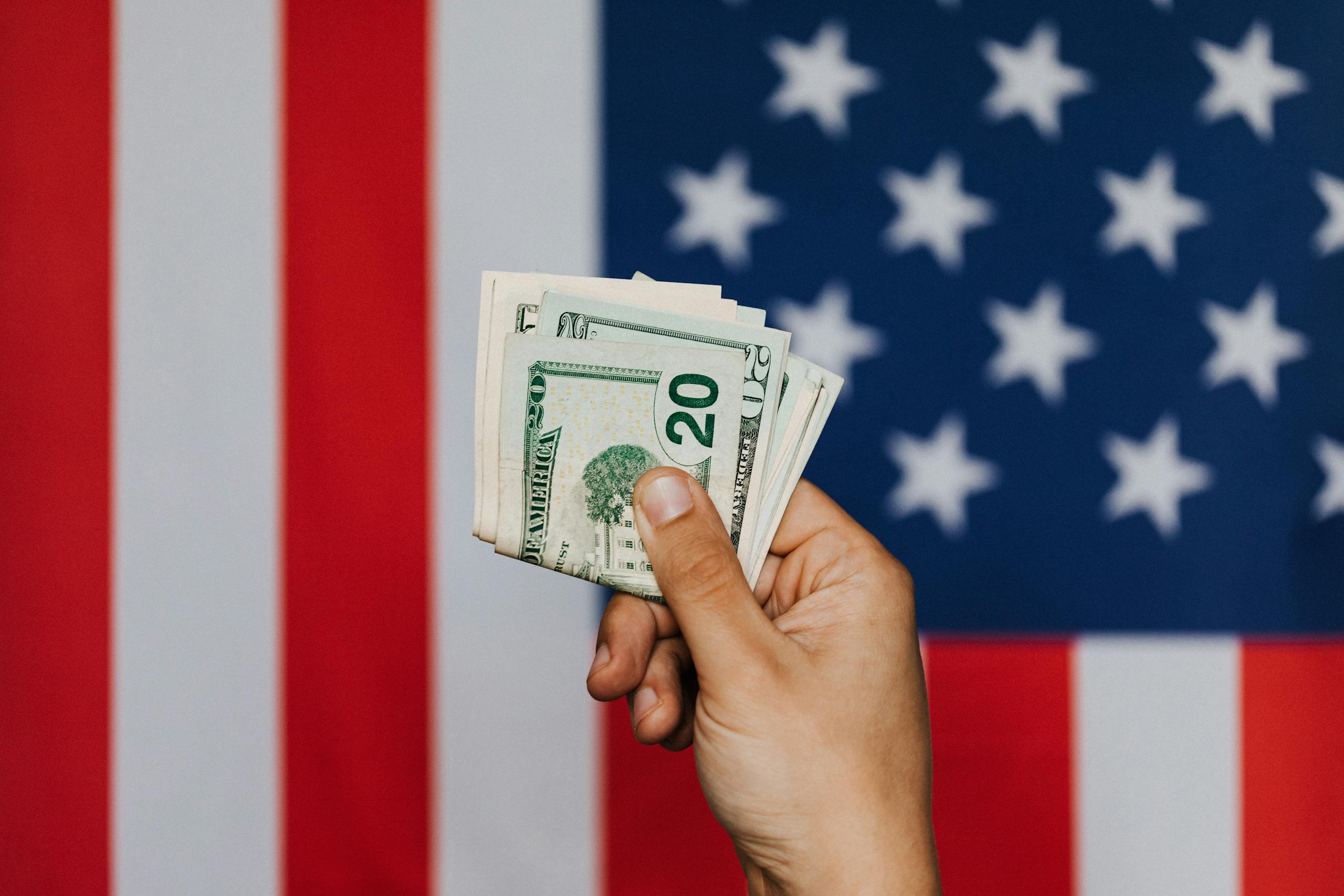 An unrecognizable male demonstrating dollars before official flag of USA on background