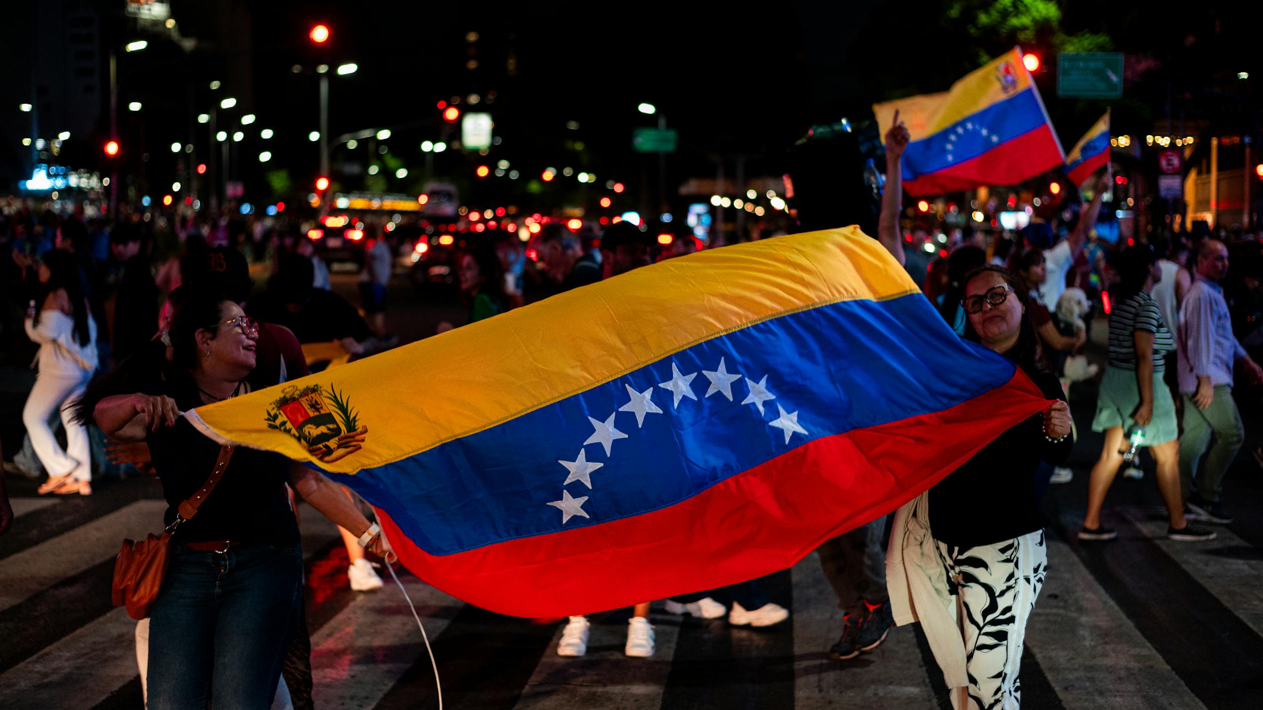 Venezuelans celebrating with national flags on a busy street in Buenos Aires at night.