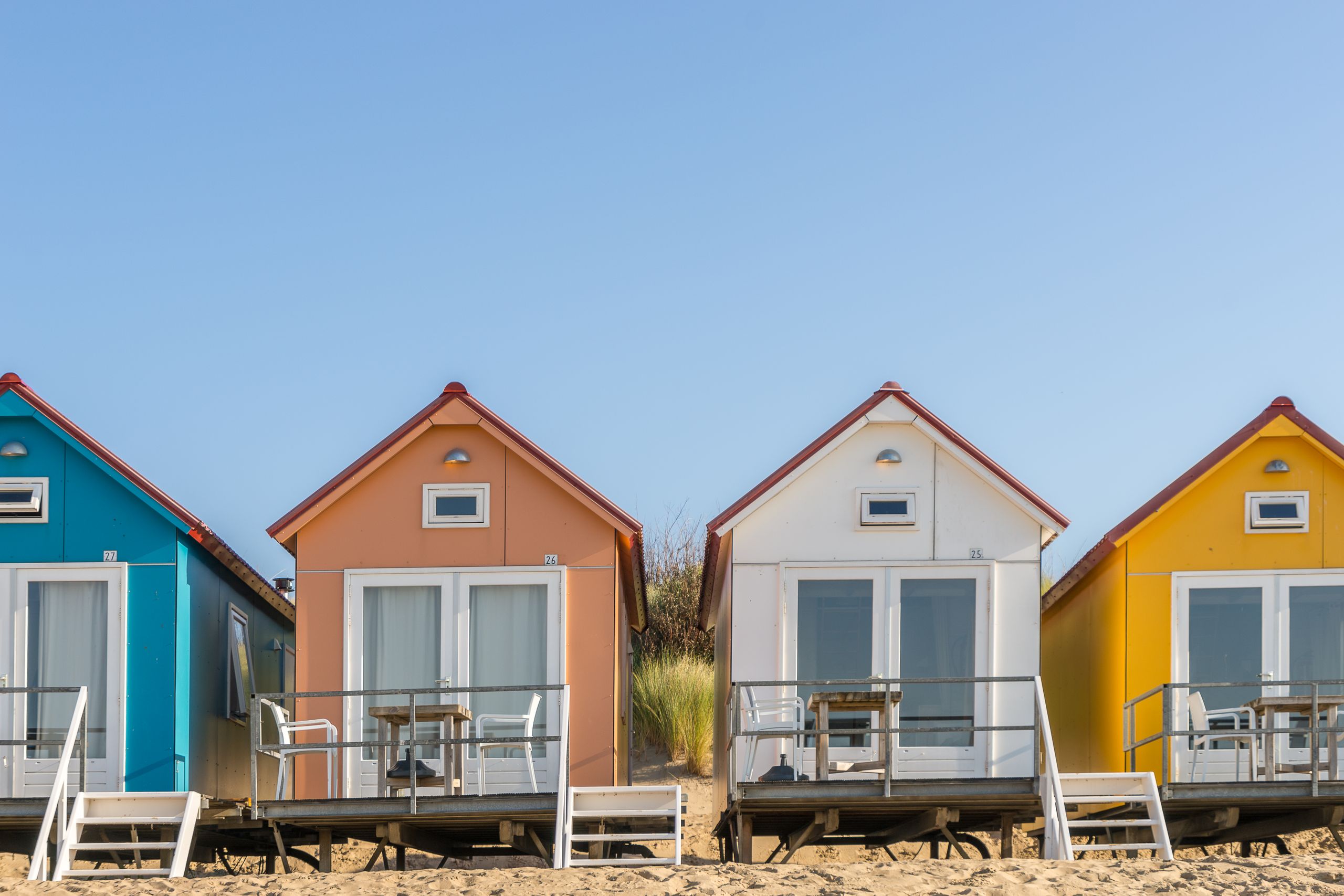 Vibrant bungalows on a sandy beach with clear blue sky, perfect for vacation vibes.