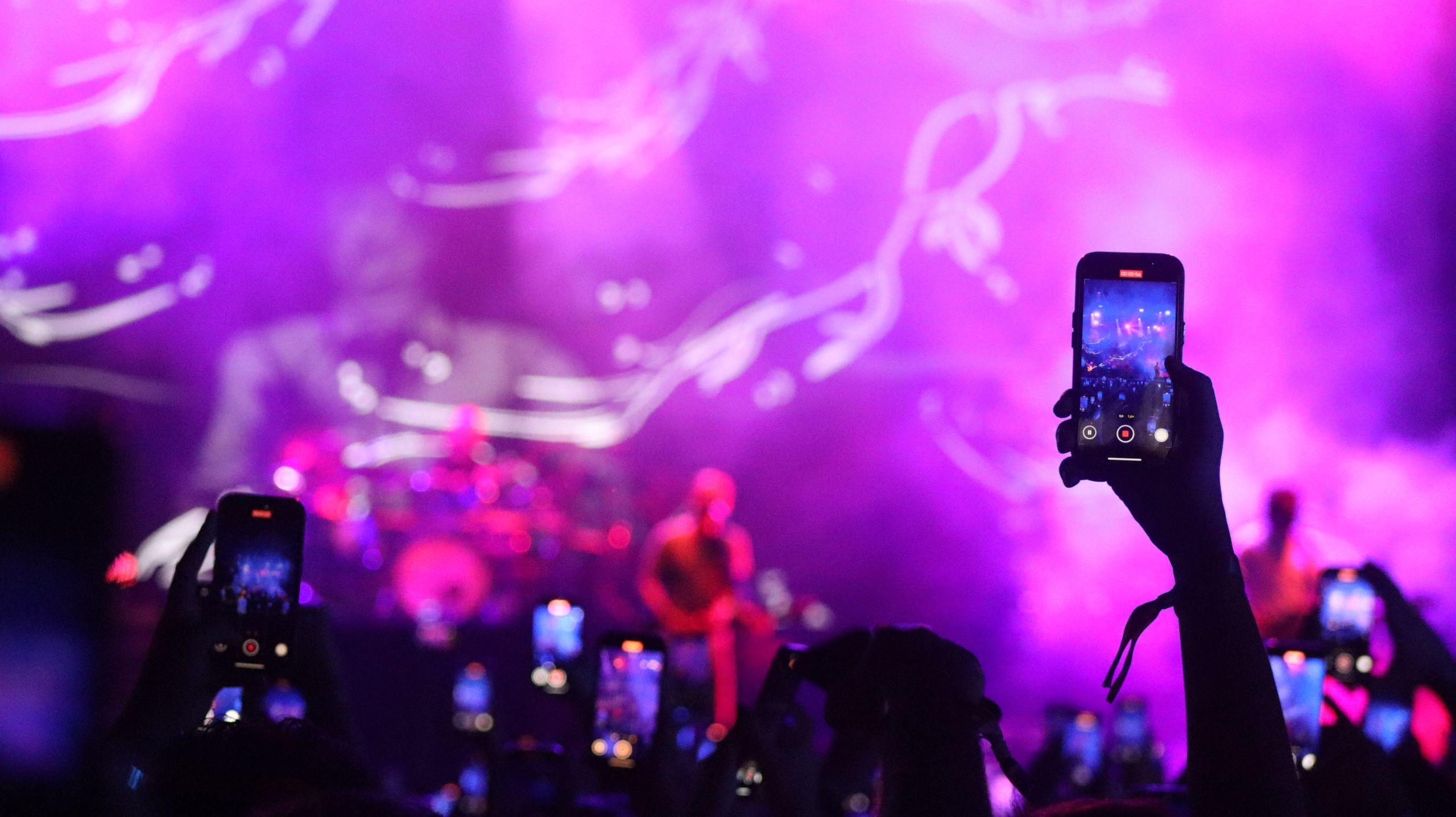 Vibrant concert with audience capturing moments on smartphones under dramatic lighting.