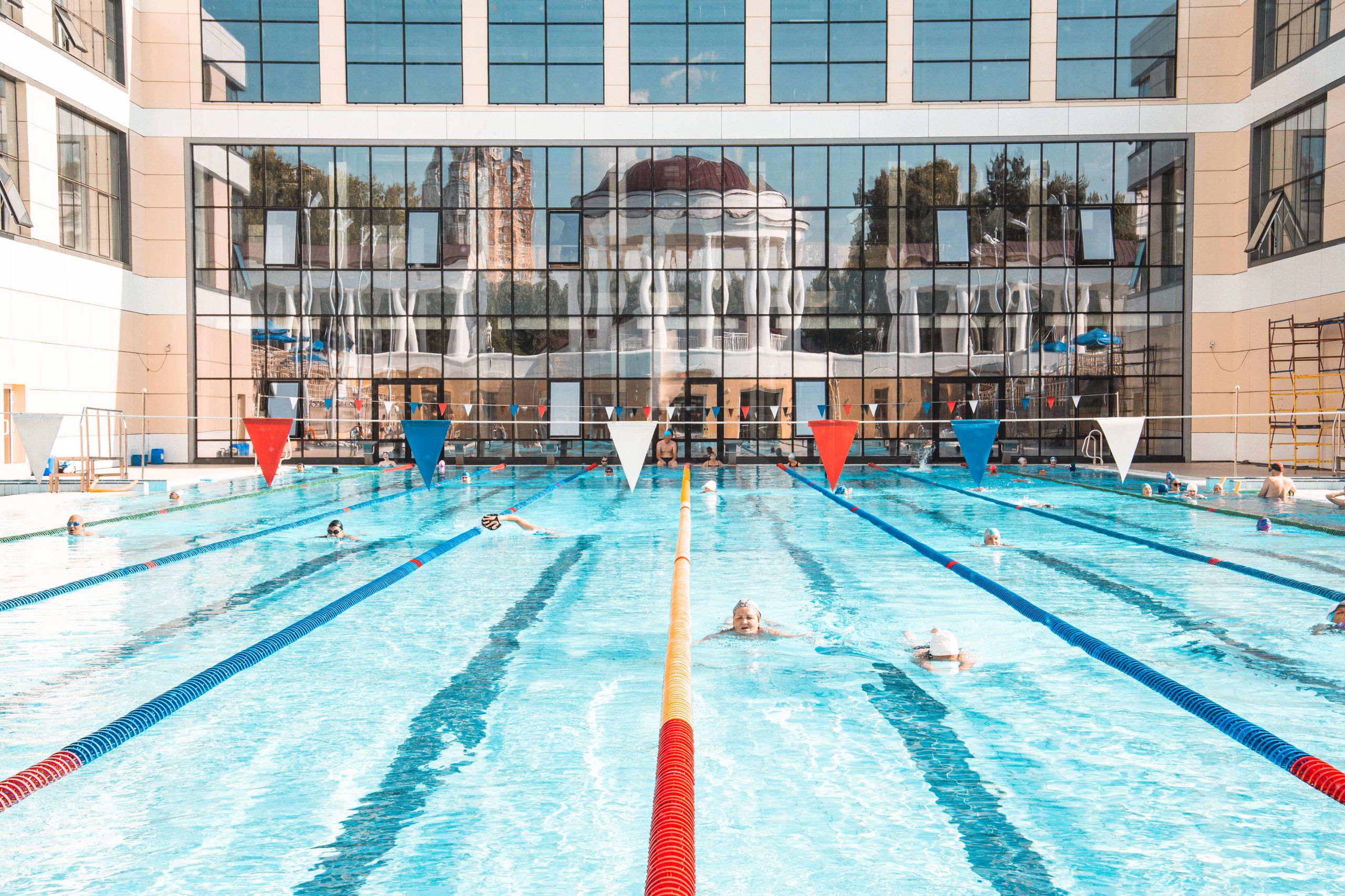Vibrant swimming pool scene with clear reflections on a building facade, capturing leisure and activity.