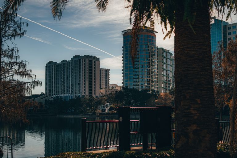 A view of Orlando's modern skyline reflecting on a tranquil lake, surrounded by trees.