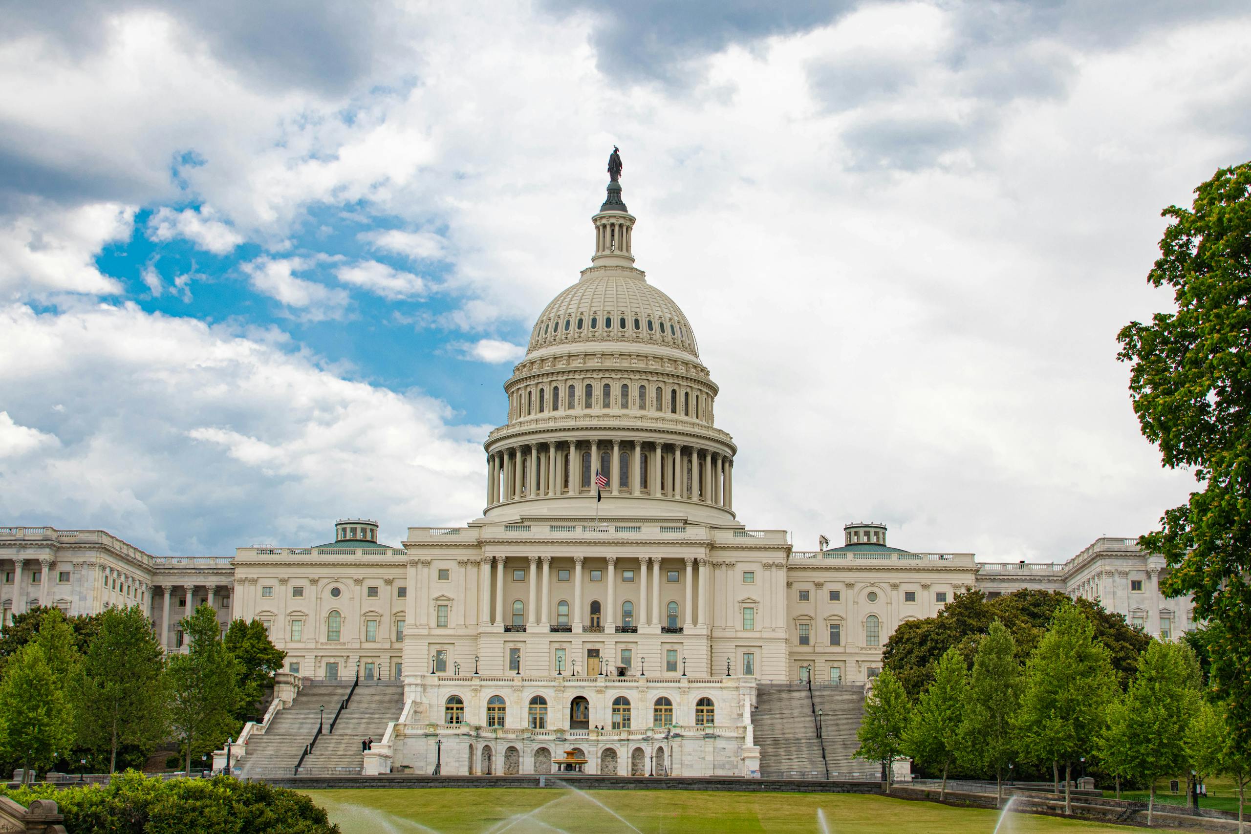 View of United States Capitol with neoclassical architecture against a cloudy sky in Washington D.C.