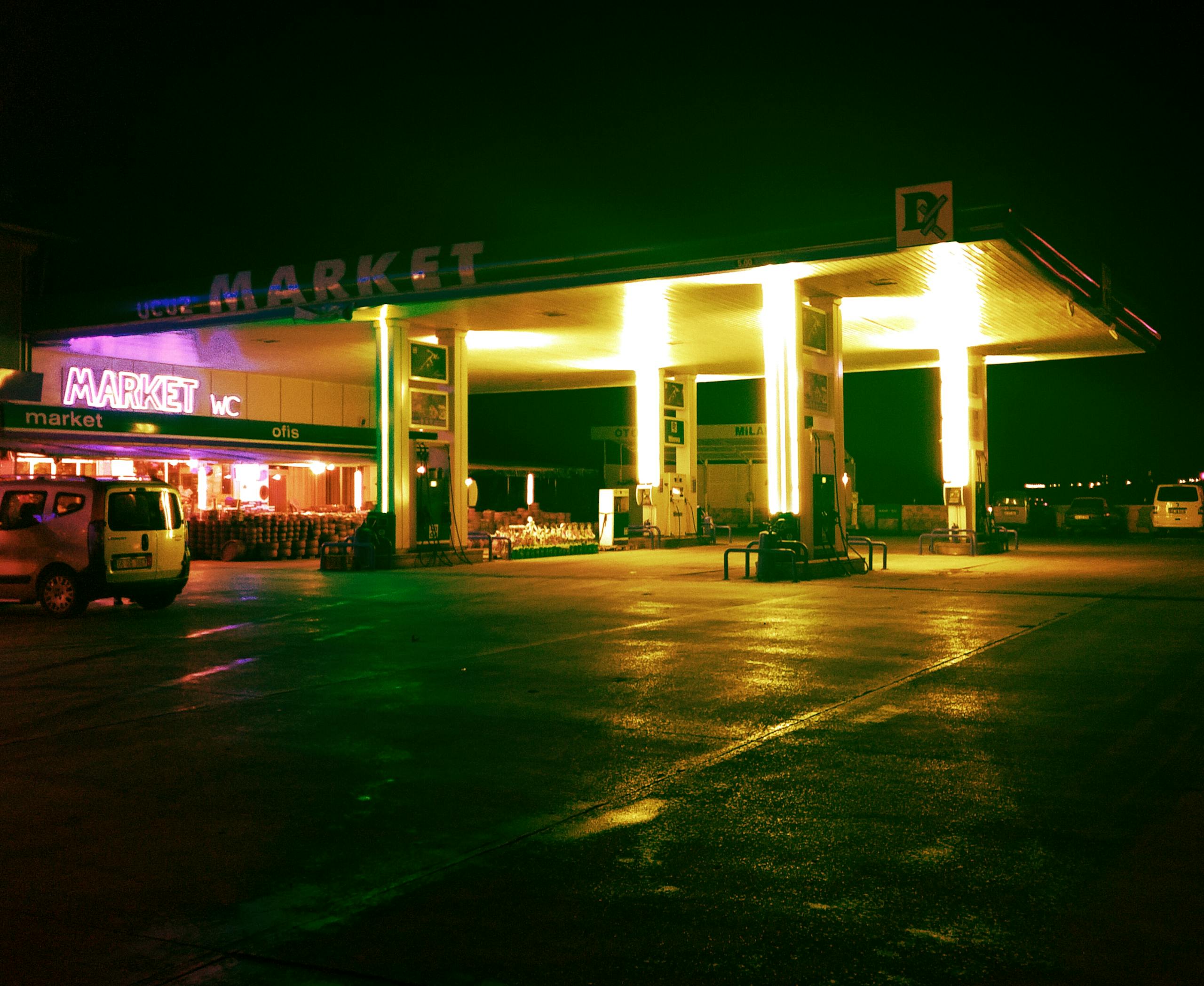 Vividly lit gas station and market during nighttime with glowing neon lights.