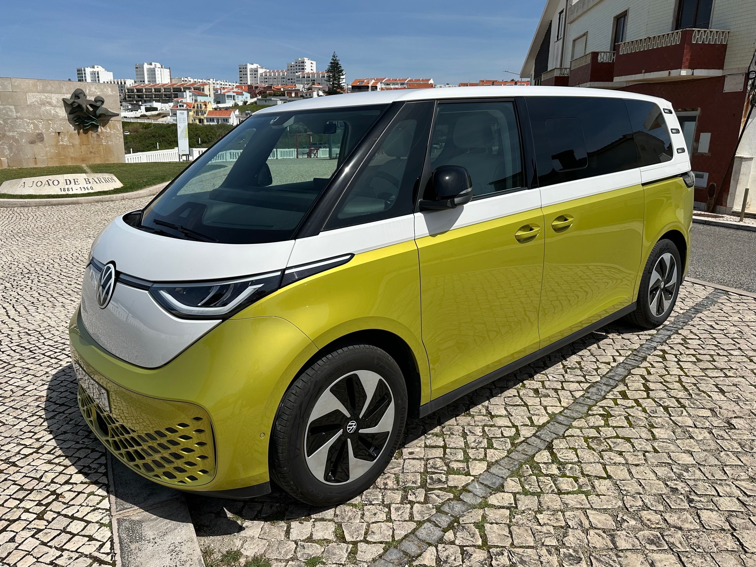 Volkswagen ID. Buzz parked on cobblestone street in scenic Portuguese town under clear skies.