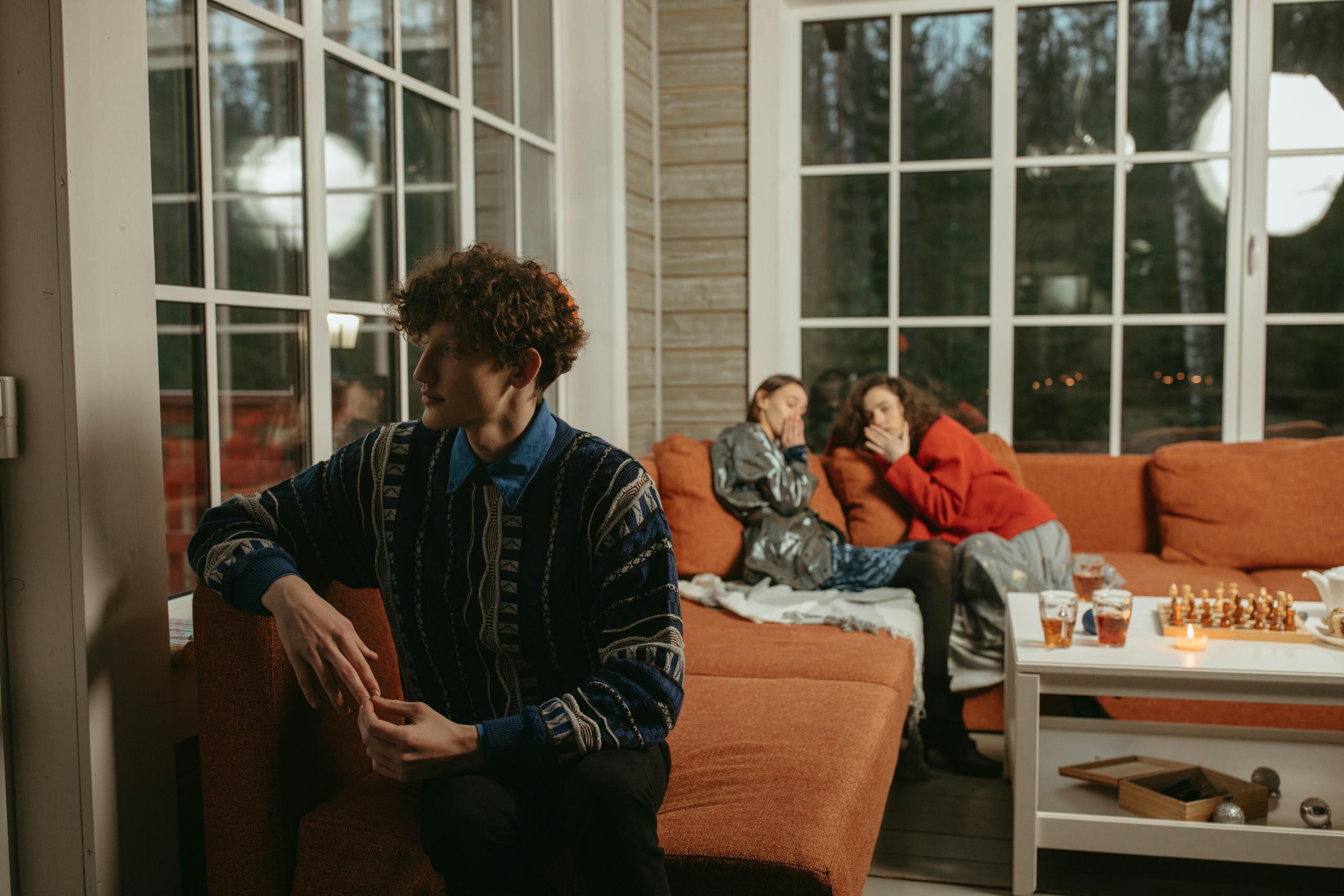 Warm and relaxed indoor gathering with friends chatting on a cozy couch by a large window.