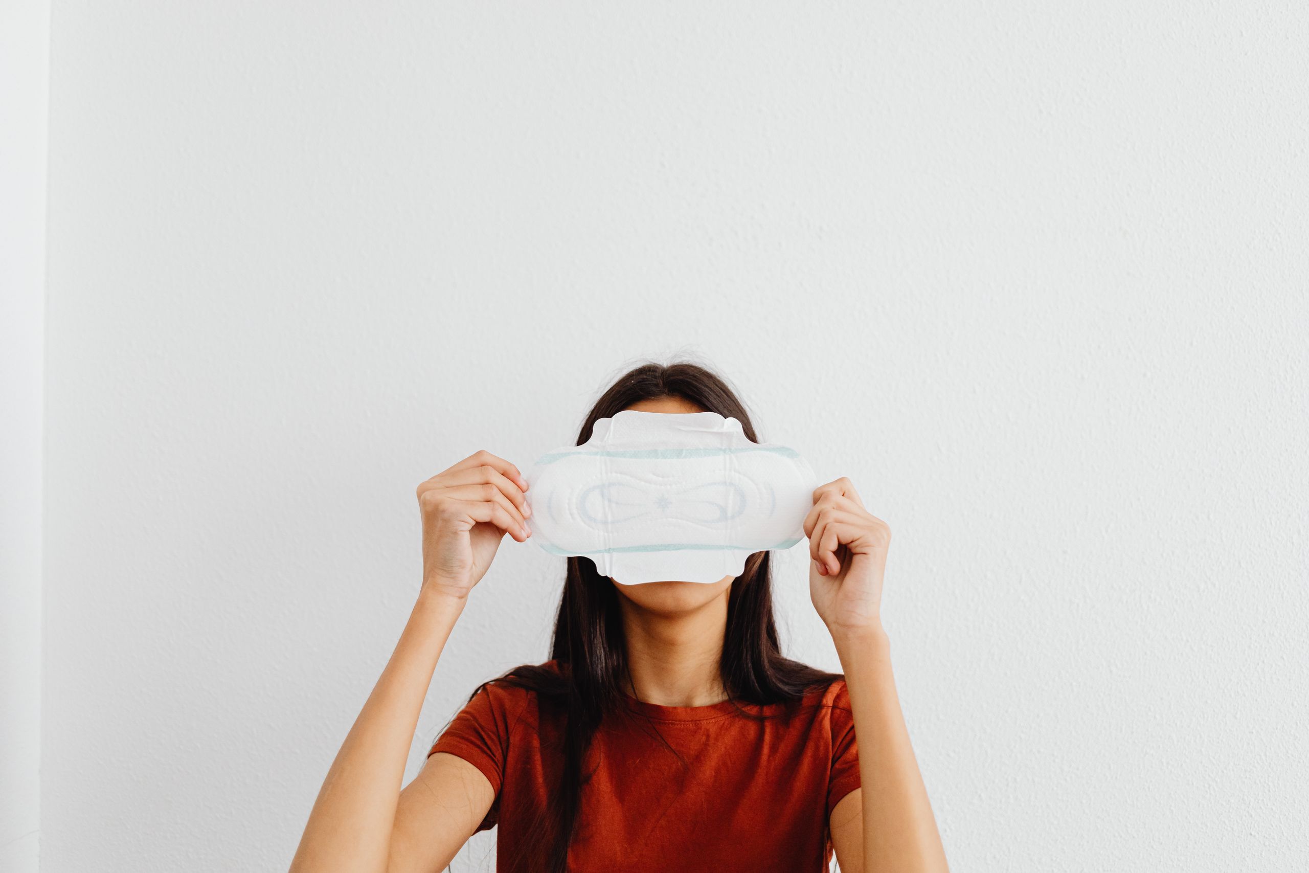 Woman concealing face with a sanitary pad against a white background.