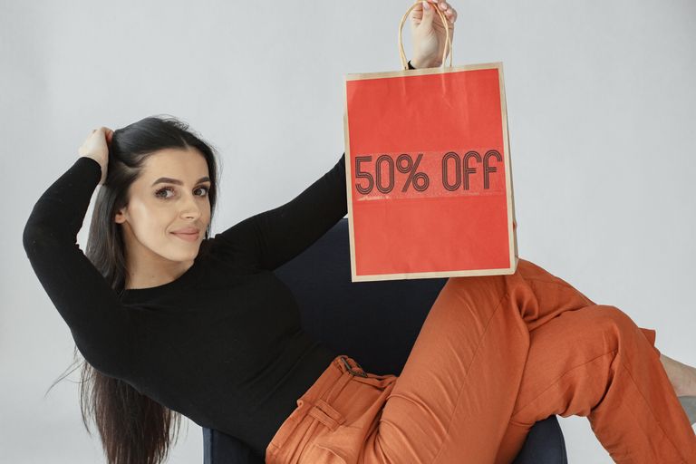Woman holding a vibrant 50% off shopping bag, promoting sales and discounts indoors.