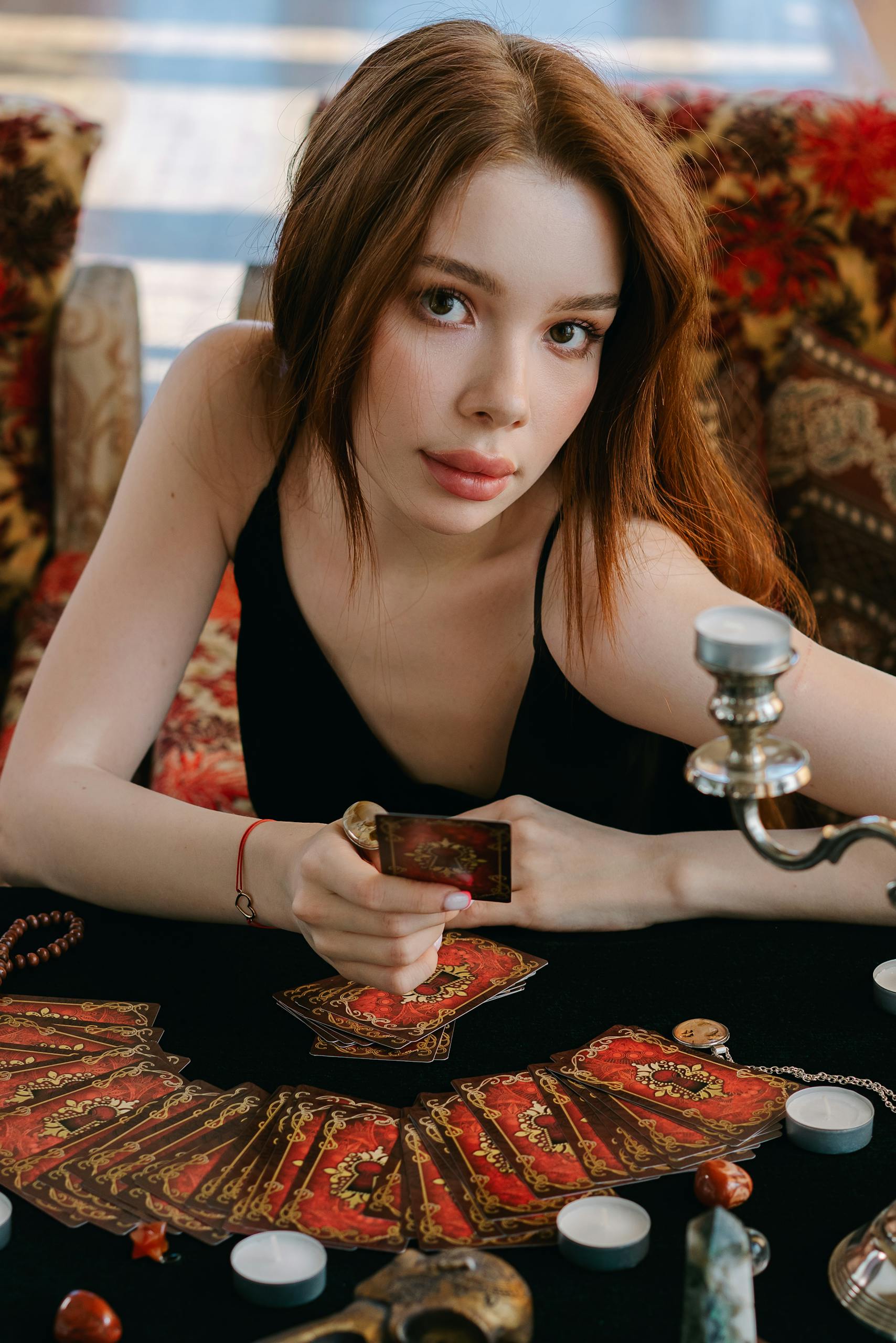Woman seated at a table holding a tarot card, evoking a mystical and spiritual atmosphere.
