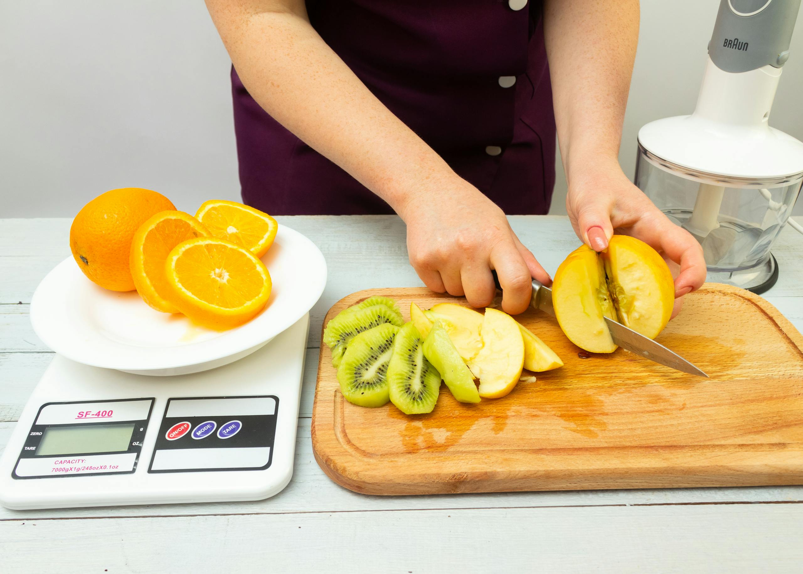 Woman slicing fruits including apple, kiwi, and orange for a healthy meal preparation.