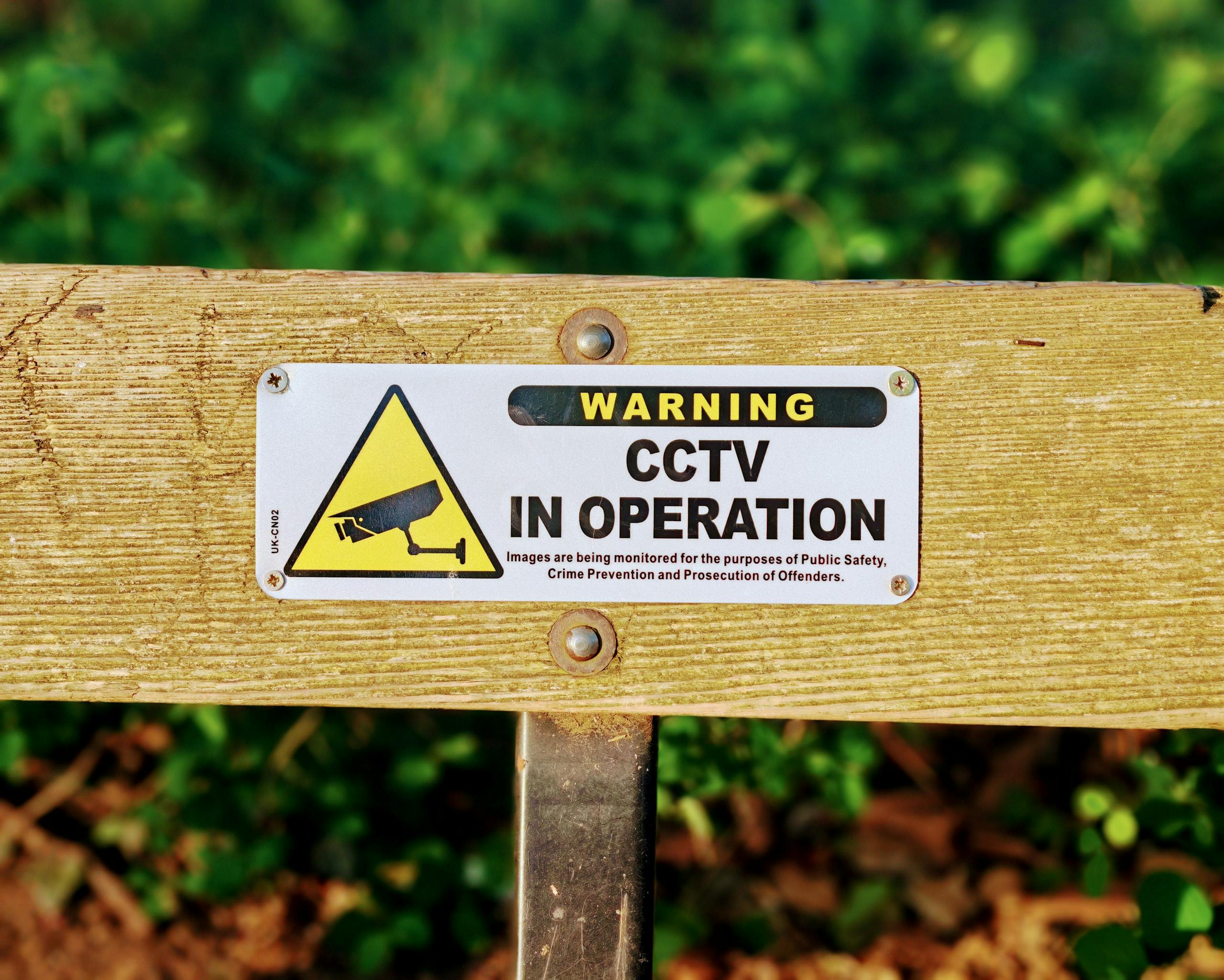 Wooden bench with a CCTV in operation warning sign, emphasizing public safety.