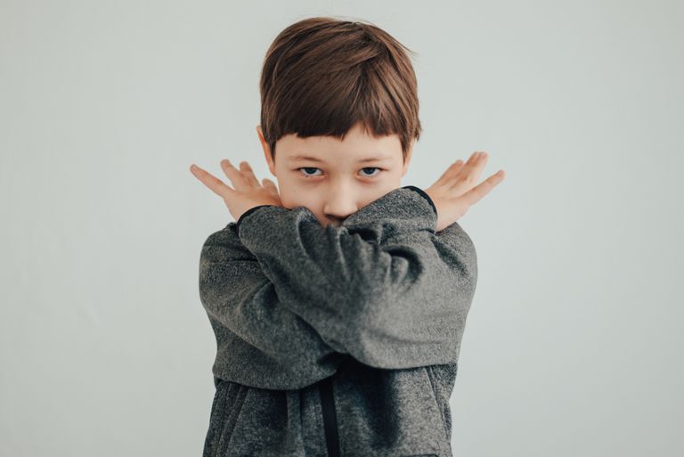 Young boy poses with arms crossed, wearing a gray sweater against a white backdrop.