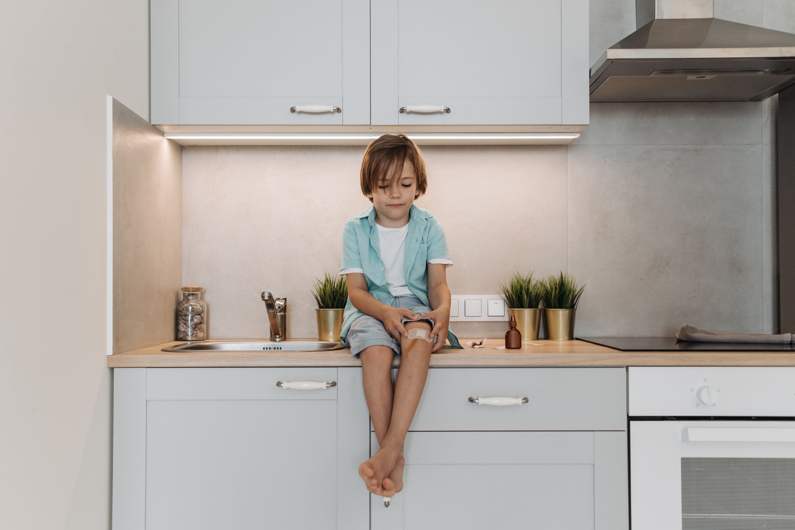 Young boy sitting on modern kitchen counter with a bandaged knee, peaceful setting.