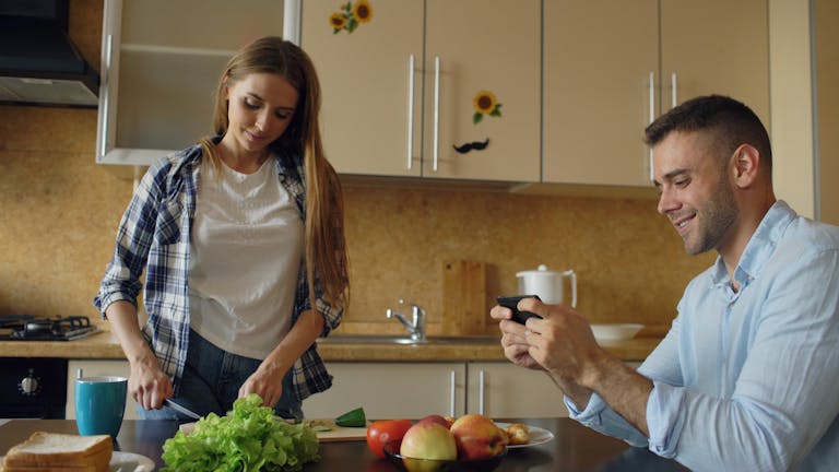 Young couple enjoying quality time cooking and photographing in a cozy kitchen.