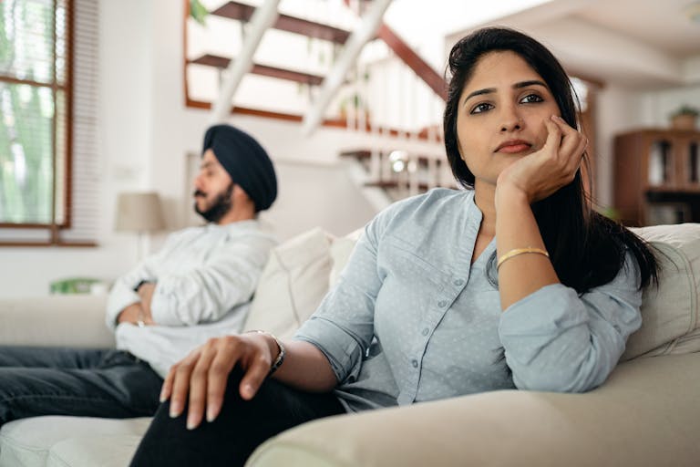 Young Indian couple sitting on different sides of couch and ignoring each other after arguing at home