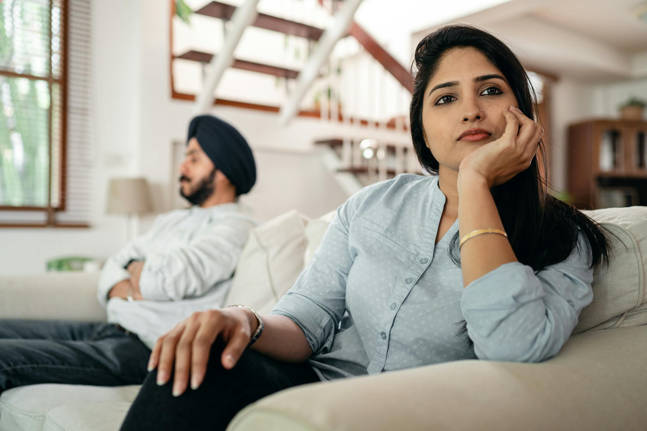 Young Indian couple sitting on different sides of couch and ignoring each other after arguing at home