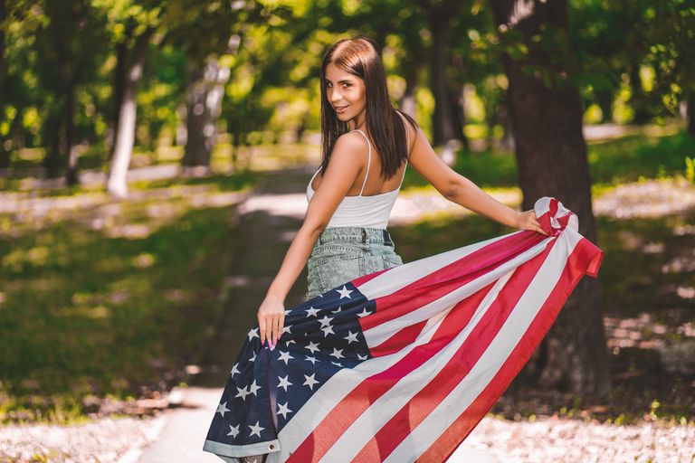 Young woman holding American flag outdoors, embracing patriotism with a smile.