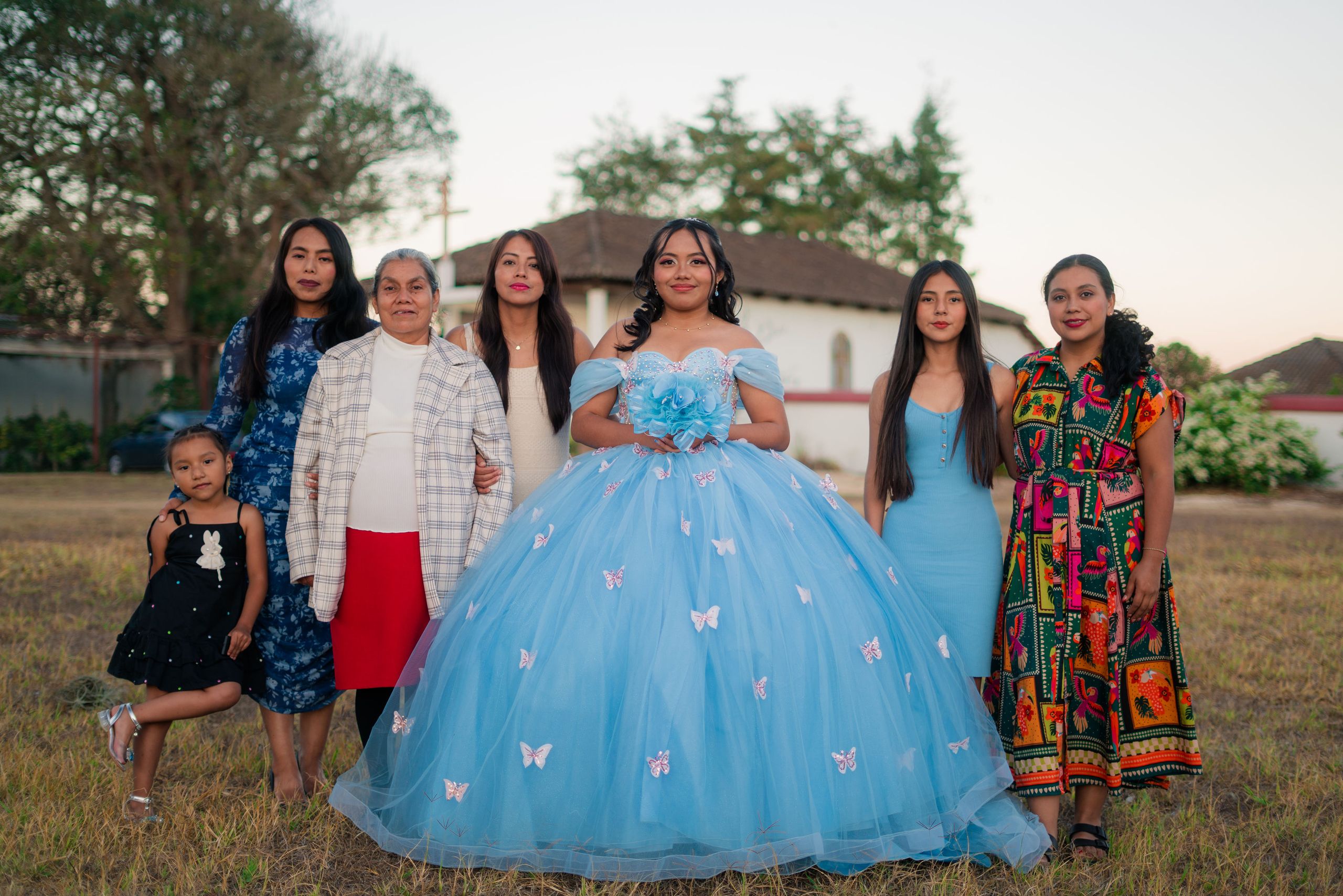 Young woman in blue quinceañera dress celebrating with family outdoors.
