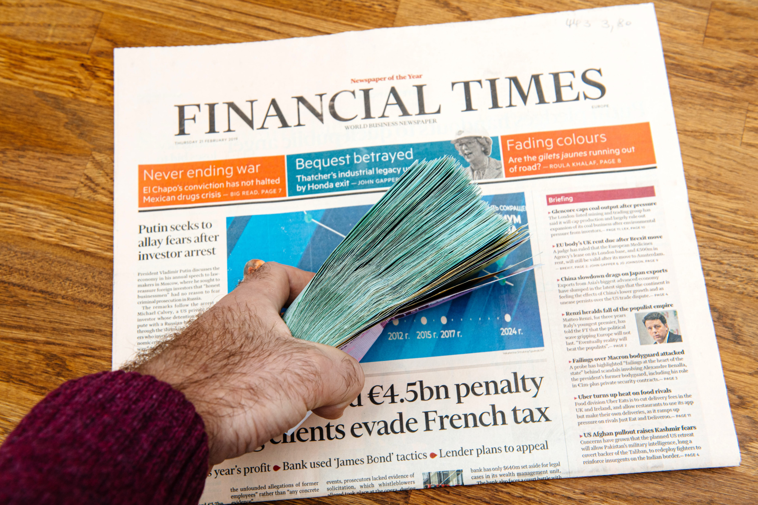 Paris, France - Mar 5, 2019: Man hand holding stack pile of thousands of Euros currency directly above the Financial Times business newspaper - wooden table background POV