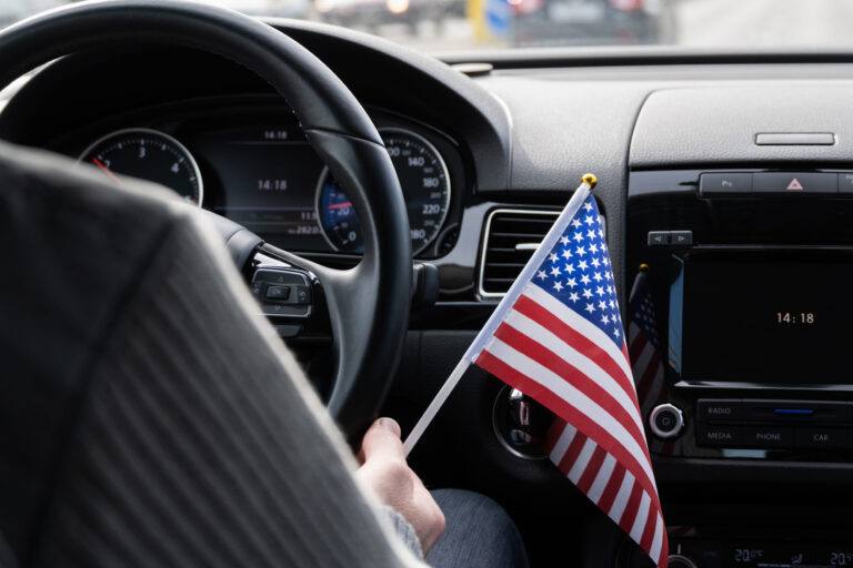 man with American flag driving a car.