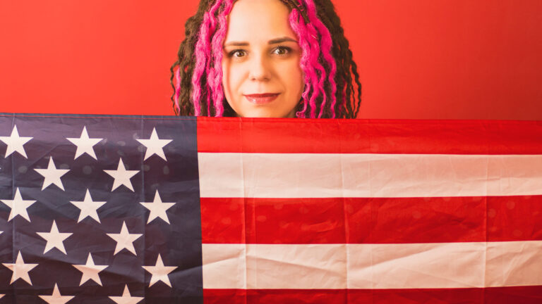 Young woman with American flag on red background. Happy female smiling and looking at camera, holding American flag
