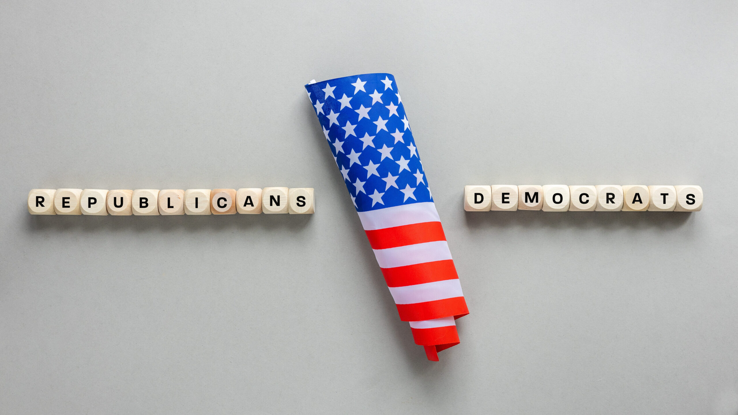 Republicans vs Democrats. Conceptual words written on wooden blocks. American flag and on the sides Republicans and Democrats. Cracked gray background, copy space, flat lay