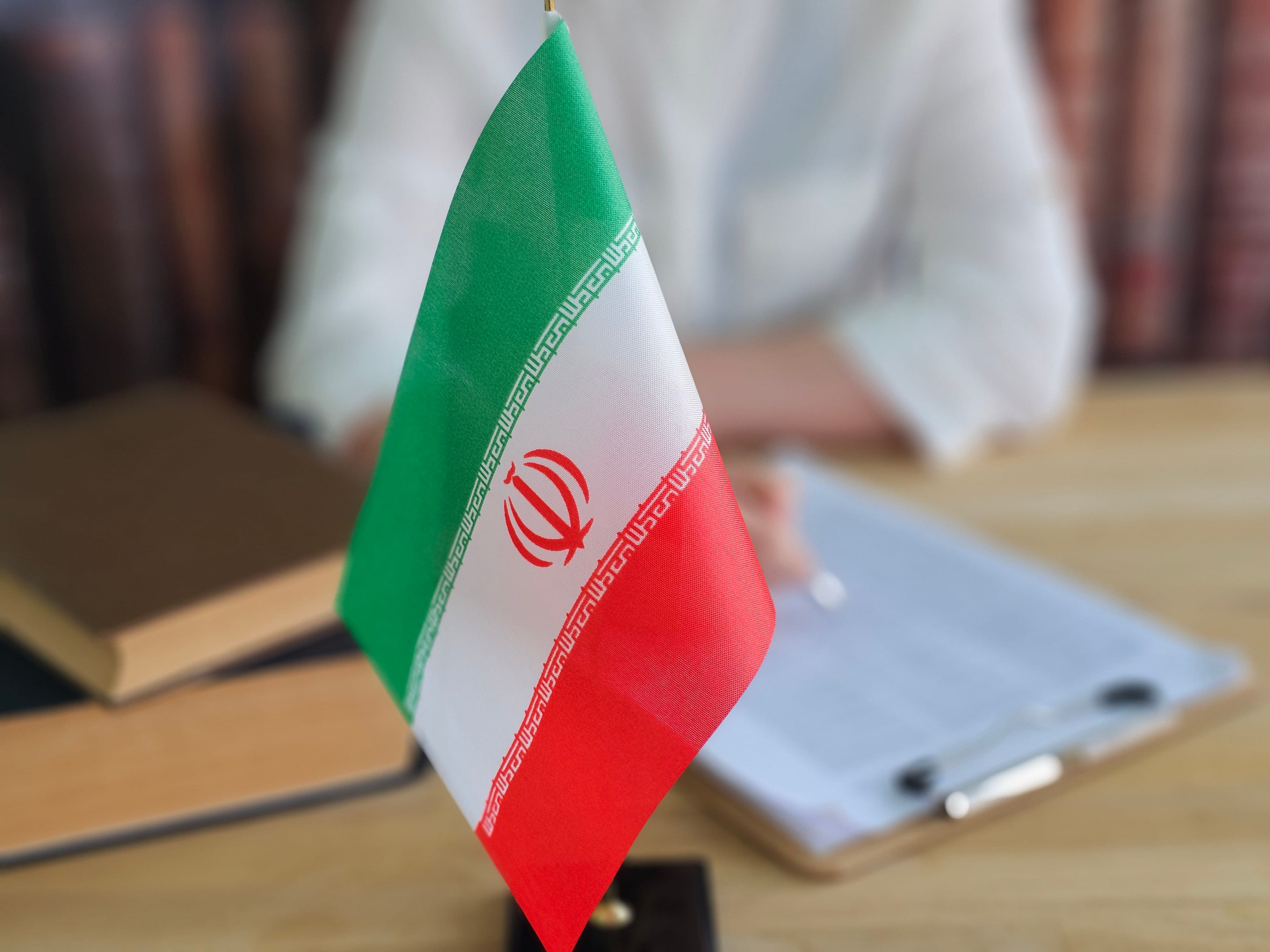 Iranian flag displayed on a desk with documents and books in the background during a meeting or discussion