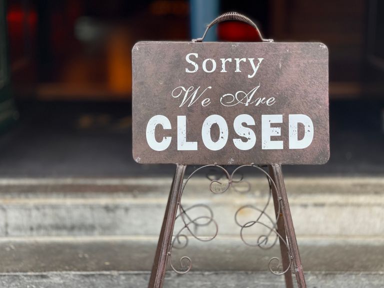 A nostalgic, metal closed sign stands at a store entrance, symbolizing closure and silence.