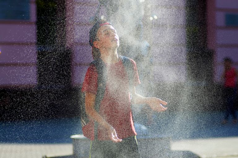 A teenage boy enjoying a refreshing water spray from a fountain on a sunny day.