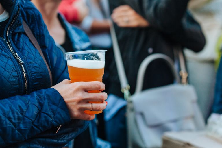 Close-up of a person holding a beer cup at an outdoor gathering, lively atmosphere.