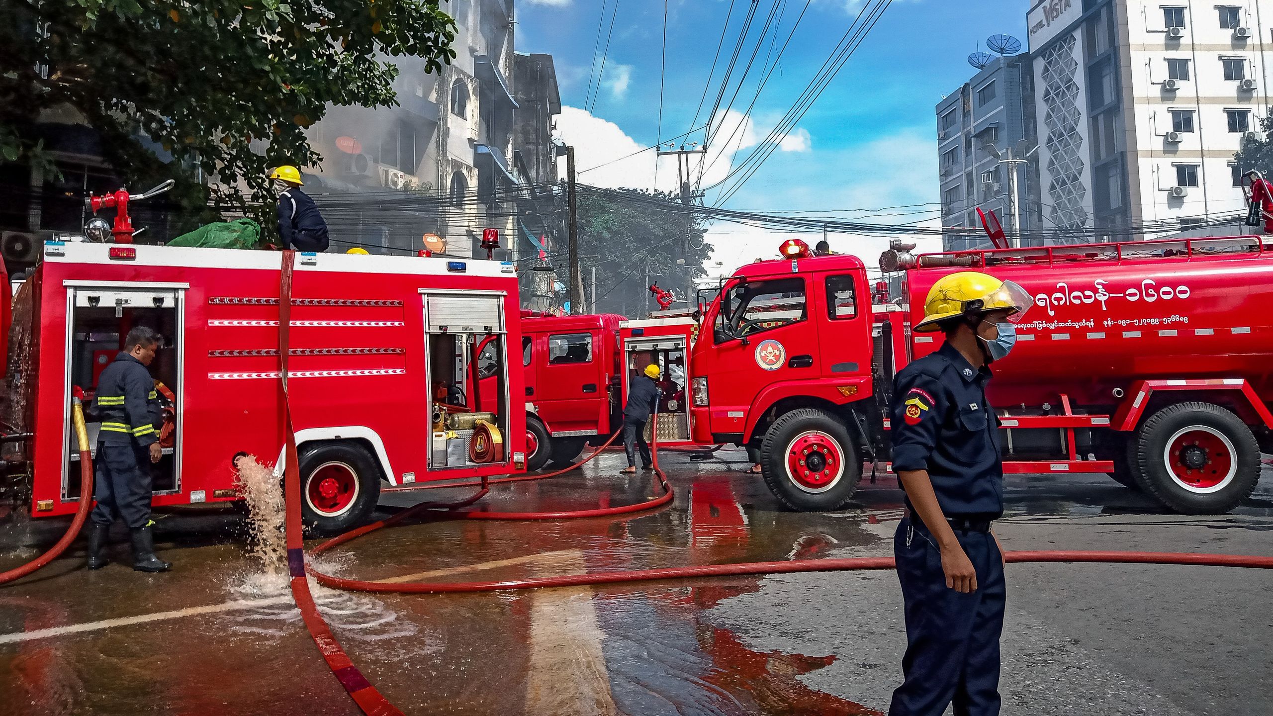 Firefighting team battling a building fire in Yangon, Myanmar with red fire trucks and hoses in action.