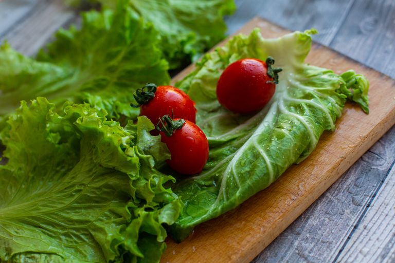 From above of various fresh lettuce leaves and ripe tomatoes placed on wooden chopping board on table in kitchen